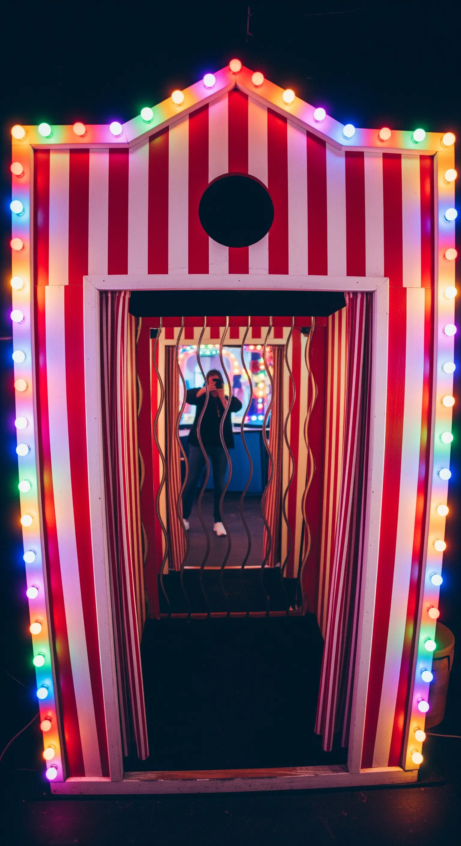 Cabina photobooth a righe bianche e rosse con luci da luna park colorate.