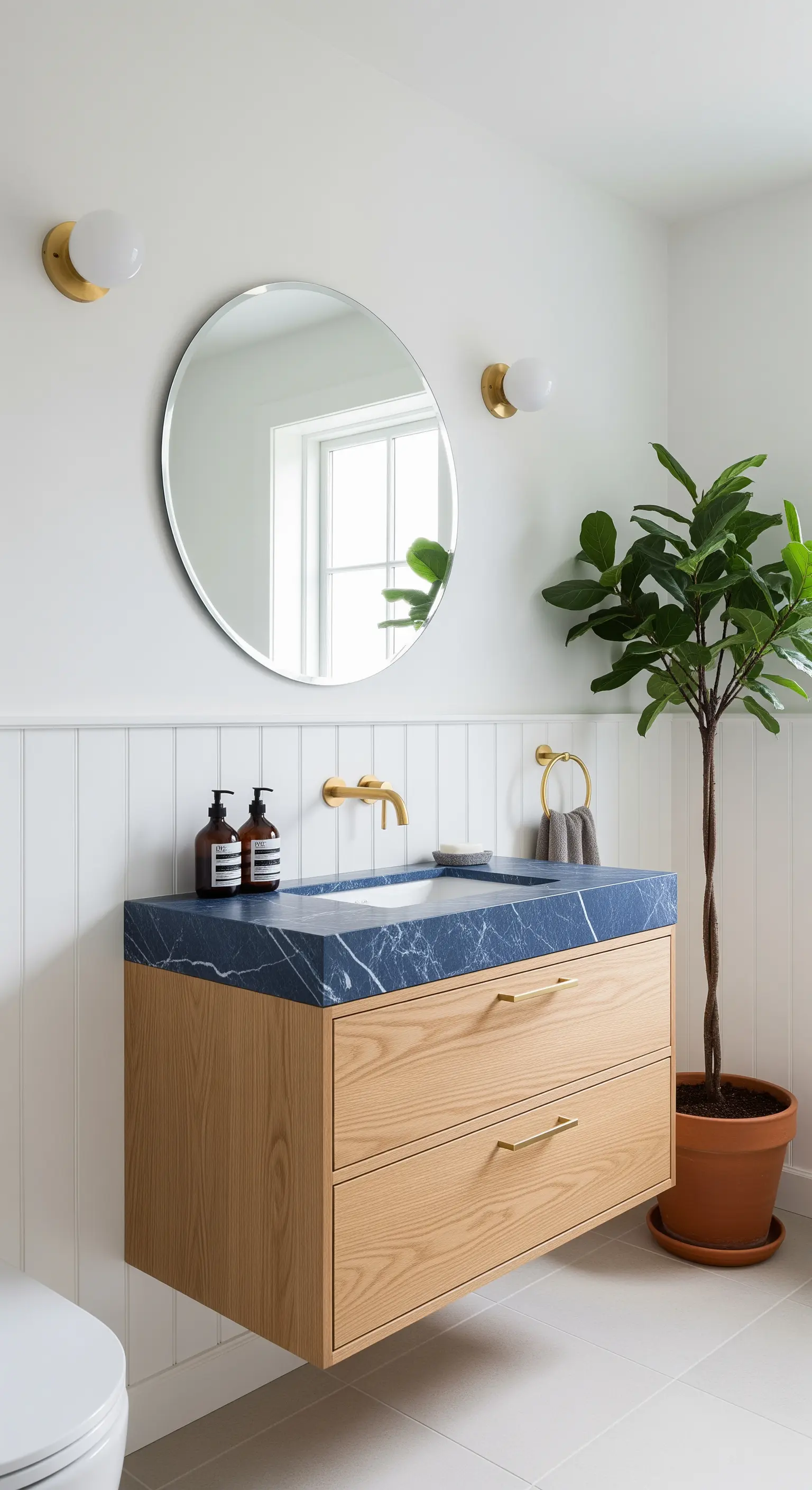 Mobile bagno sospeso in legno chiaro con top in marmo blu, specchio rotondo e boiserie bianca.