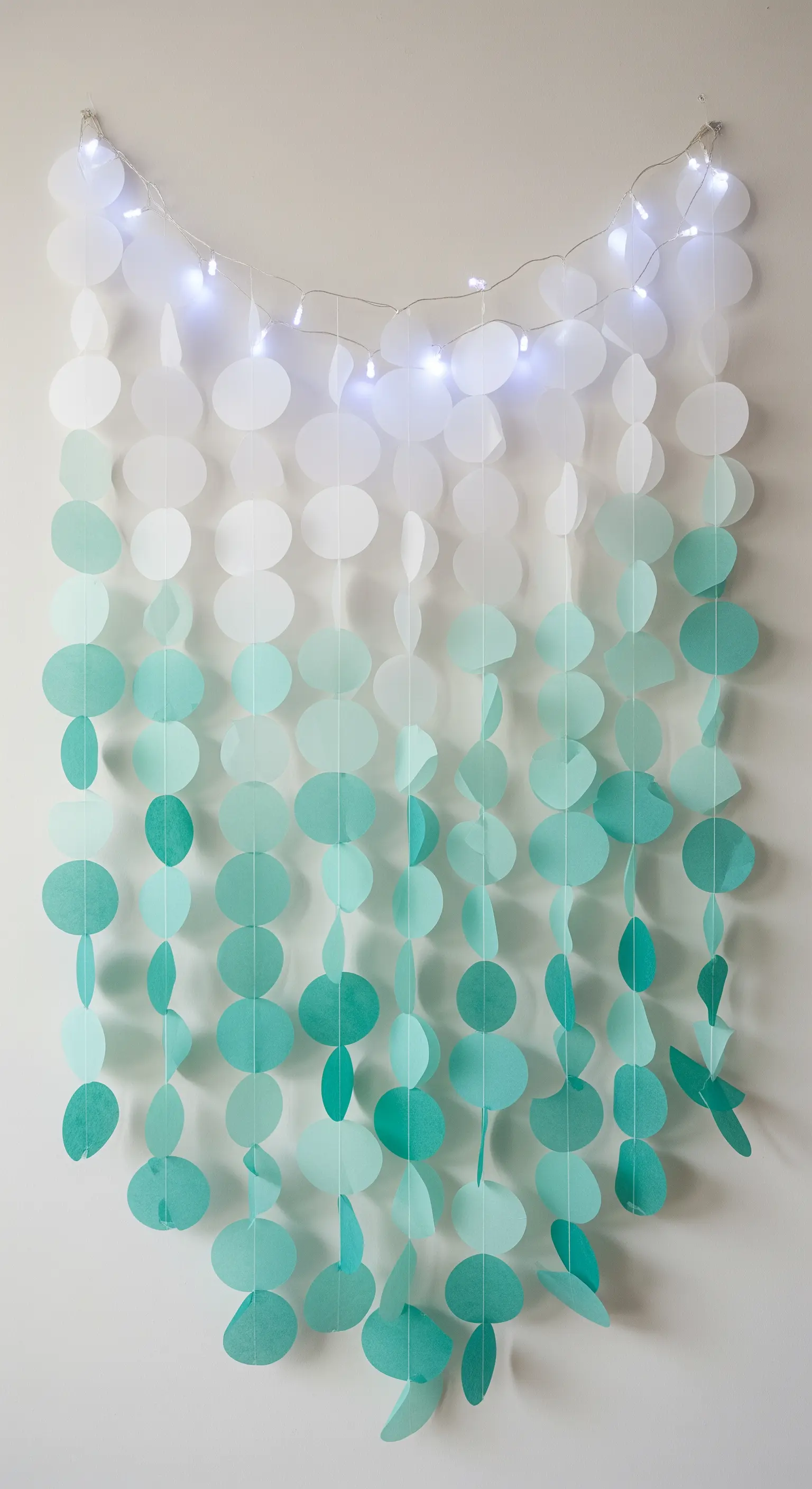 Cascata verticale di cerchi di carta in gradiente dal bianco al verde acqua, con luci bianche.