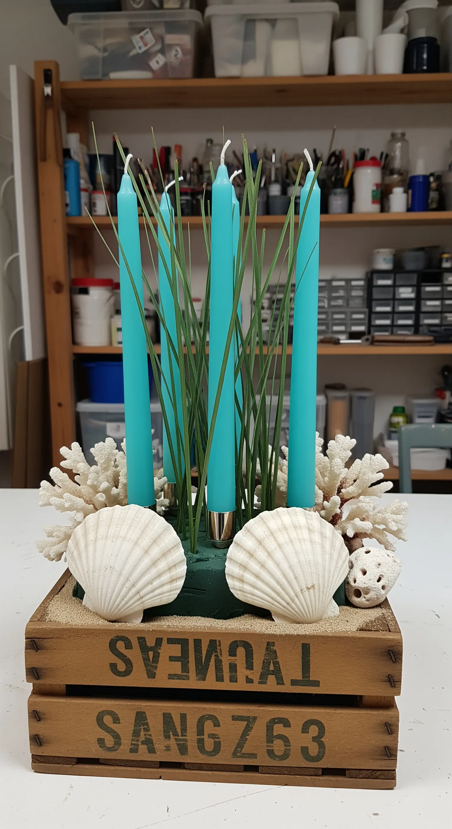 Centrotavola in una cassa di legno con candele turchesi, erba, coralli bianchi e conchiglie.