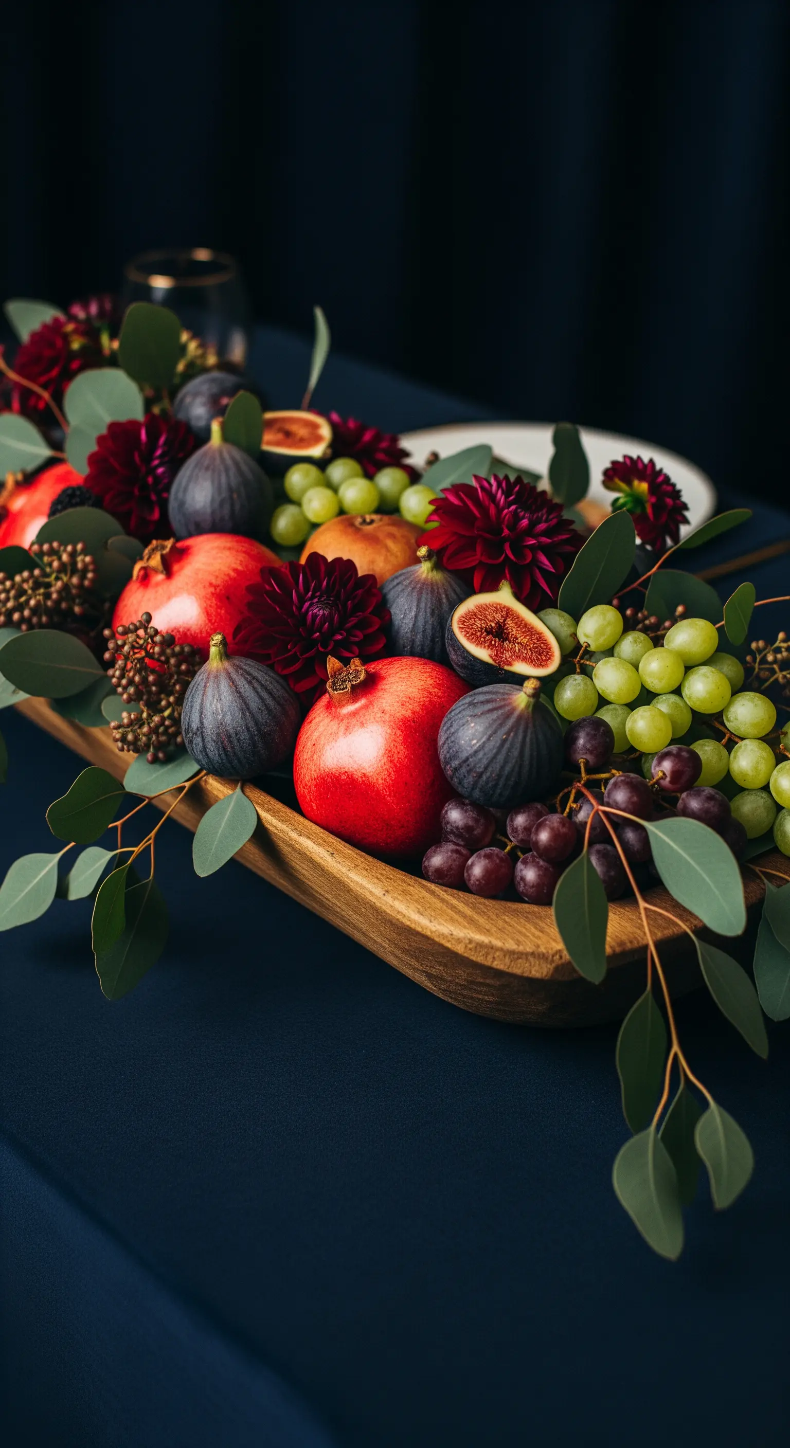 Centrotavola abbondante con melograni, fichi, uva, dalie e foglie di eucalipto.