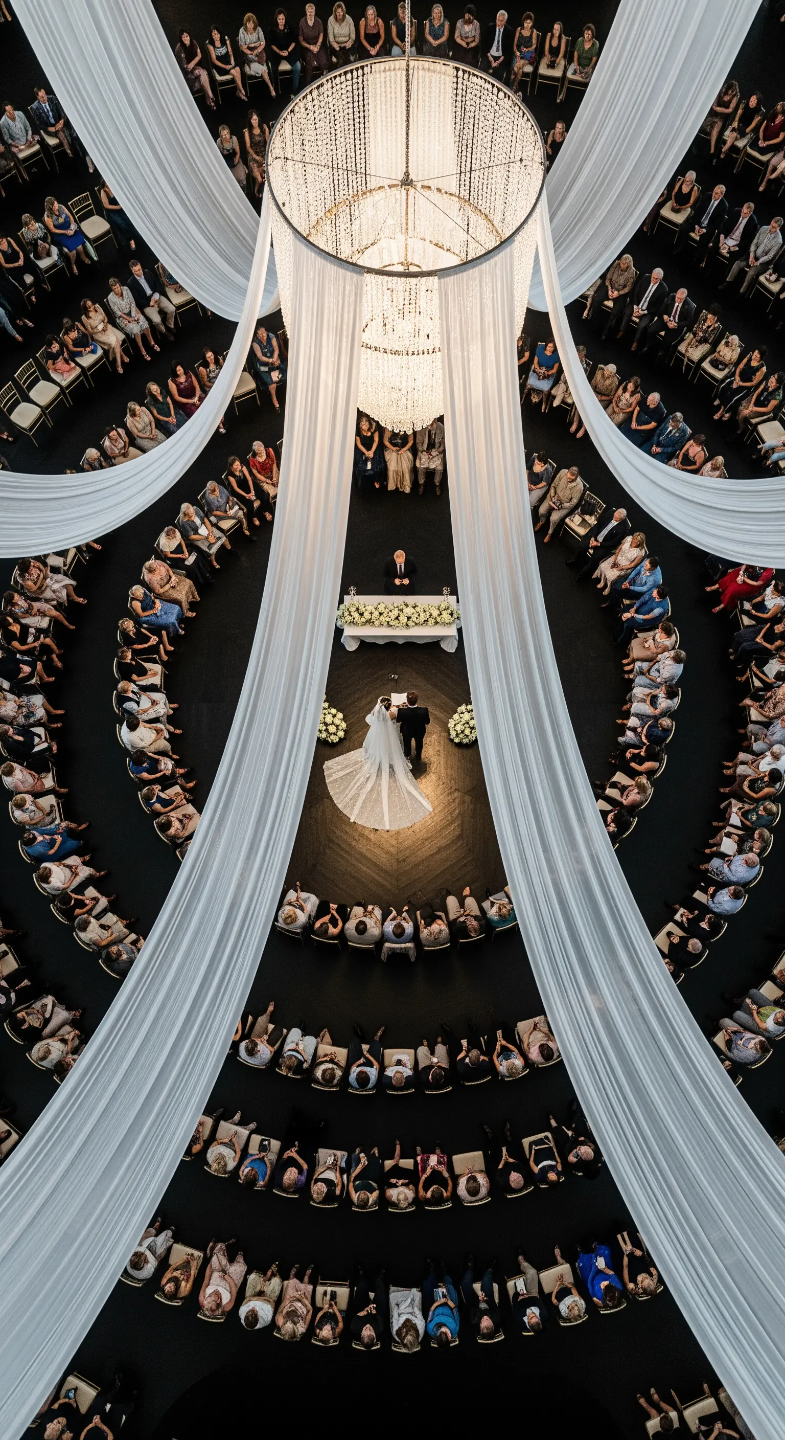 Vista dall'alto di una cerimonia nuziale circolare con un grande chandelier e drappi di seta al centro.