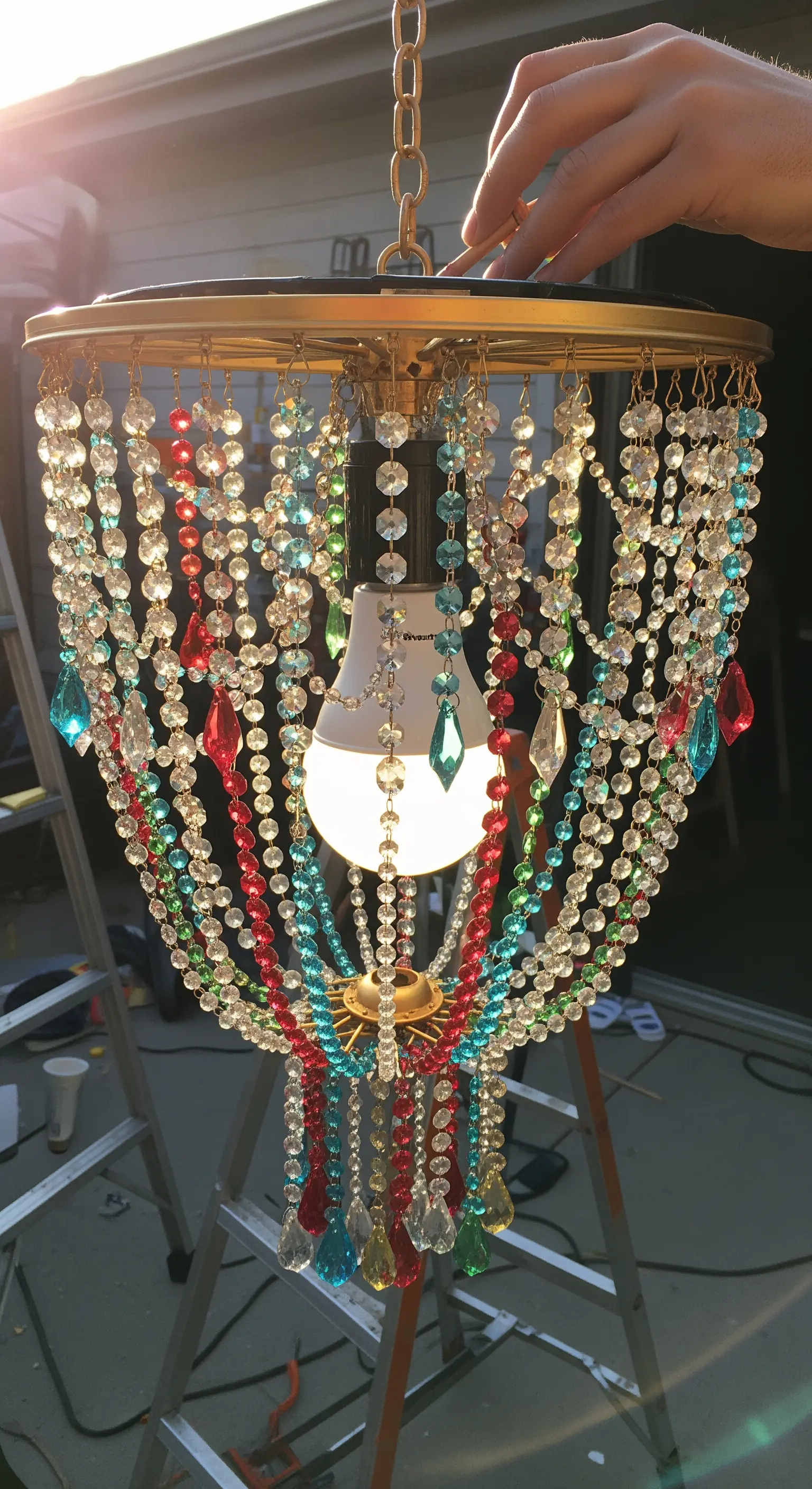 Lampadario fai-da-te realizzato con fili di perline colorate e una lampadina solare centrale.