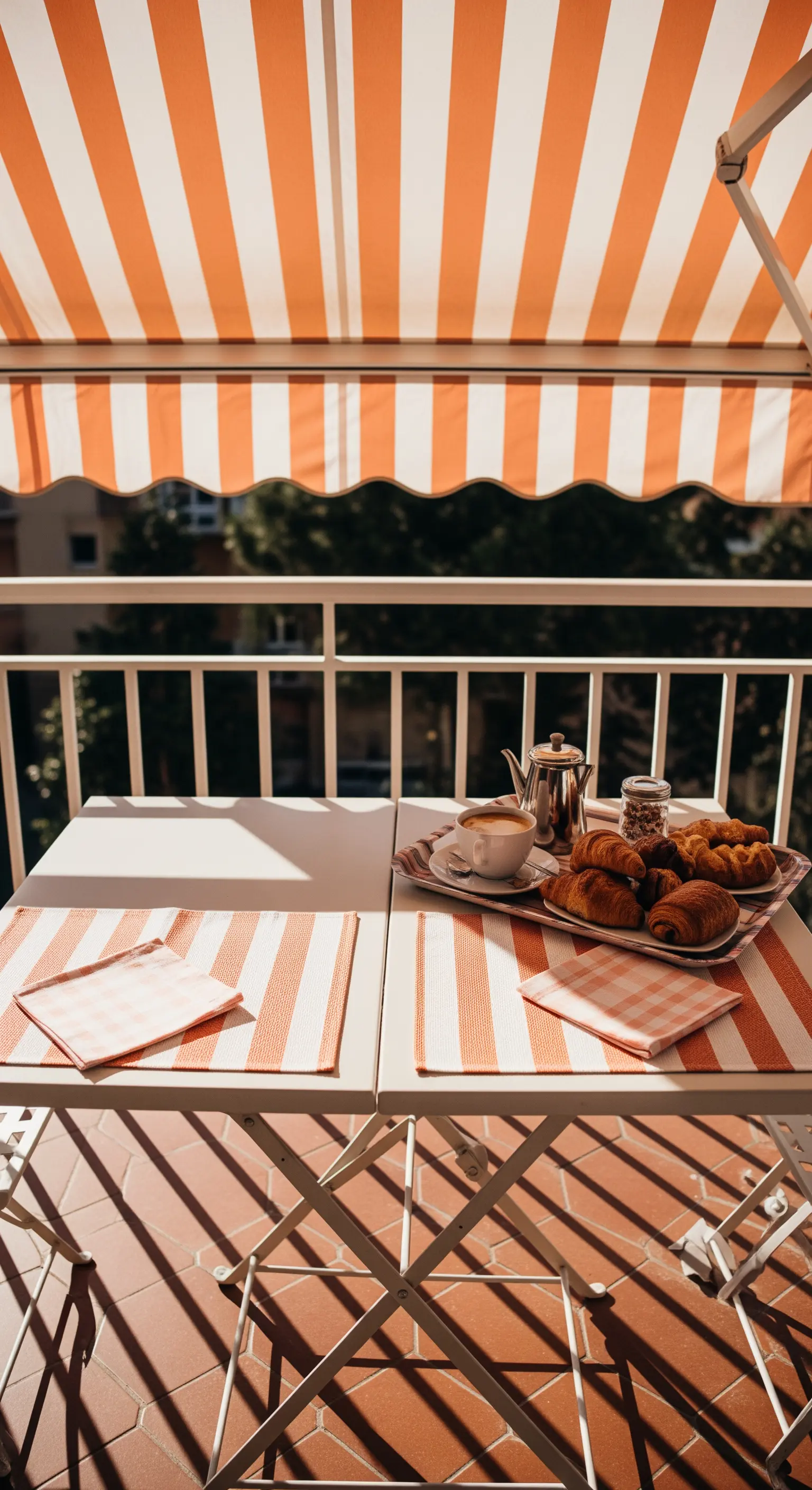 Colazione su un balcone con tenda a righe arancioni e tovagliette coordinate.