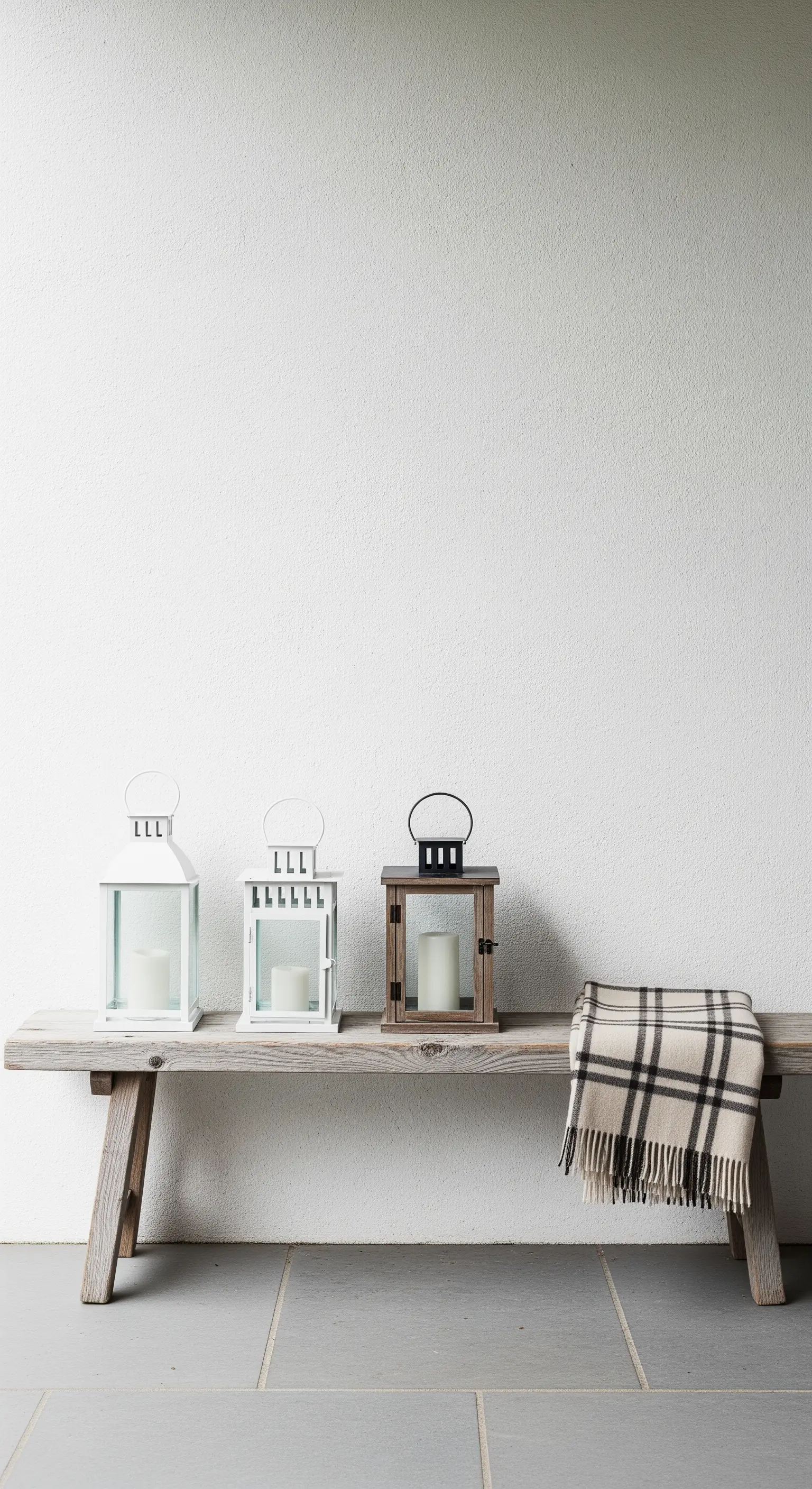 Panca in legno rustico con tre lanterne di stili diversi e un plaid a quadri.
