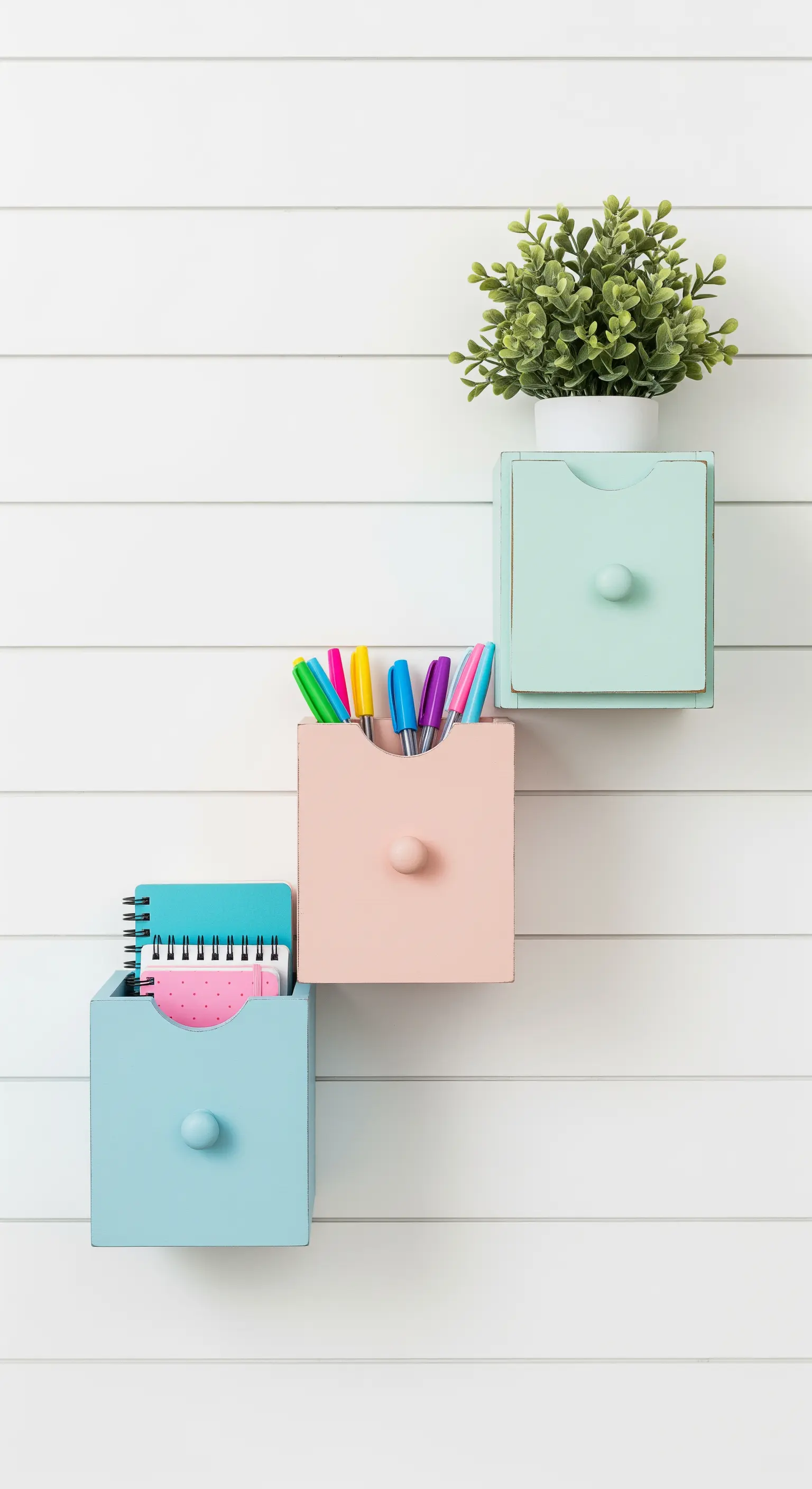 Tre piccoli cassetti color pastello montati a parete in verticale per organizzare la cancelleria.
