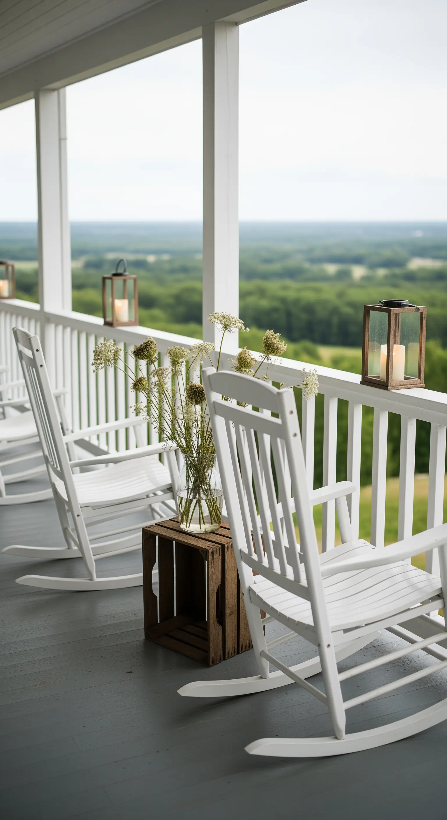 Due sedie a dondolo bianche affacciate su un paesaggio, con fiori di campo su una cassetta.