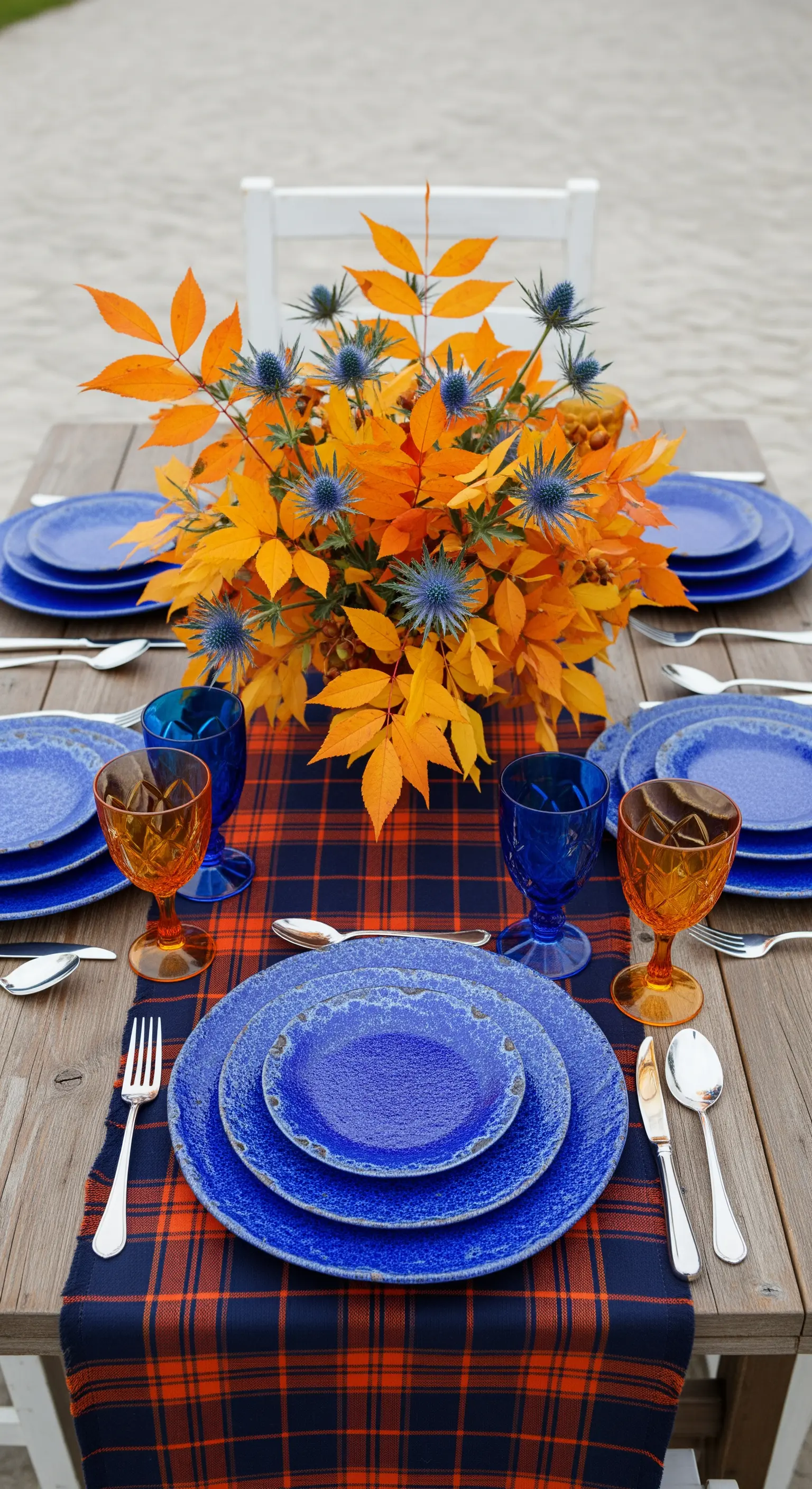 Tavola con runner tartan blu e arancione, piatti blu cobalto e un centrotavola di foglie arancioni.