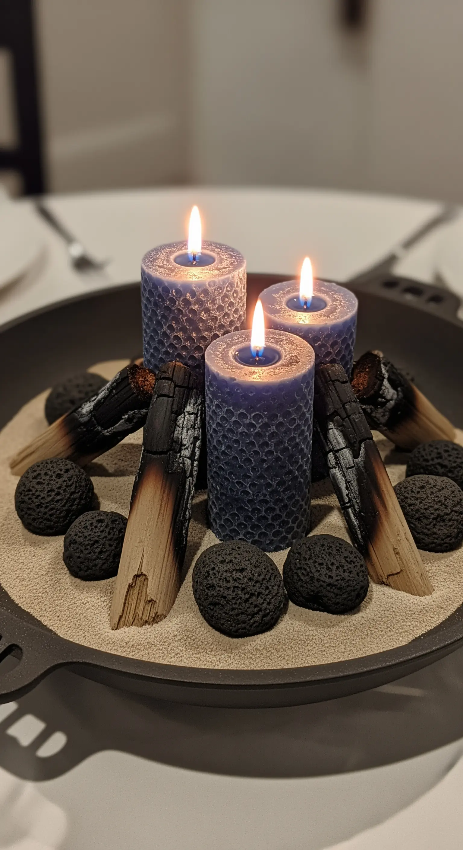 Braciere con sabbia, candele blu testurizzate, legno bruciato e pietre laviche.