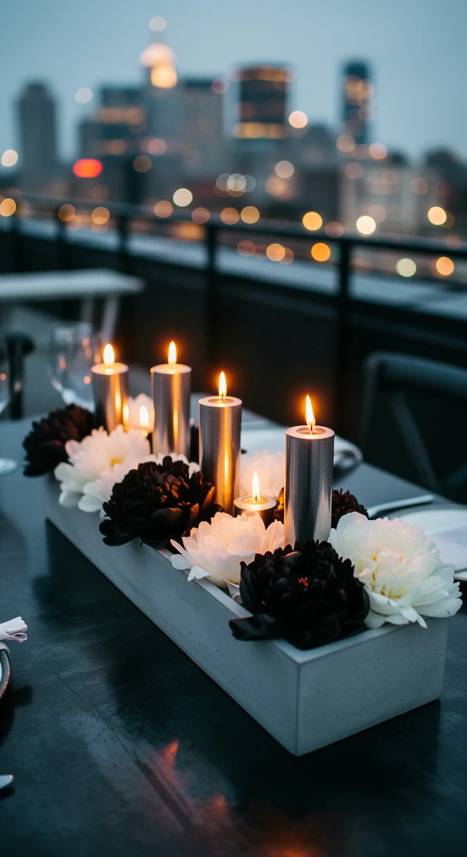 Fioriera in cemento con peonie bianche e nere e candele a colonna color argento.