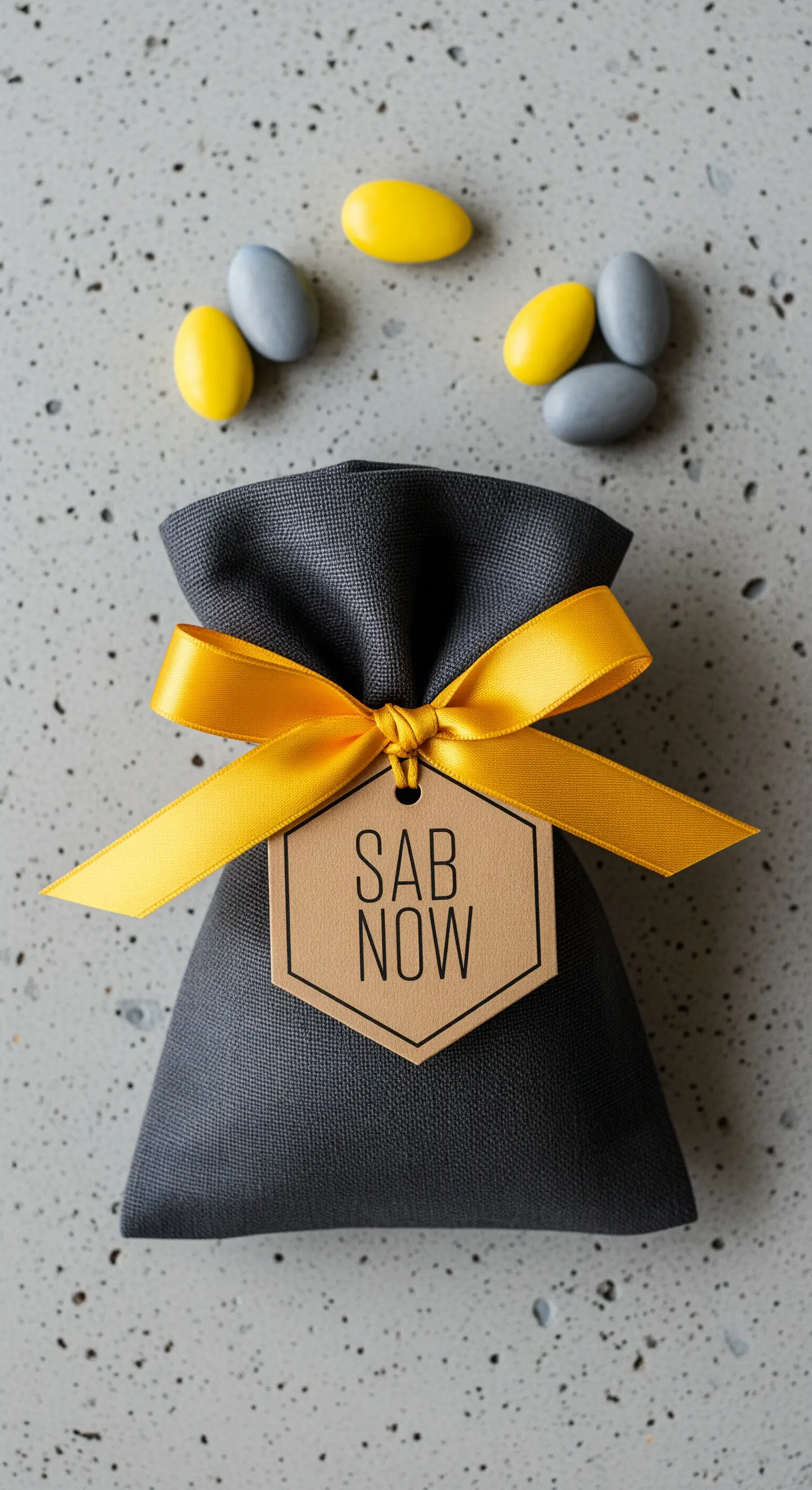 Sacchetto bomboniera in lino grigio scuro con un nastro giallo acceso e un tag esagonale moderno.