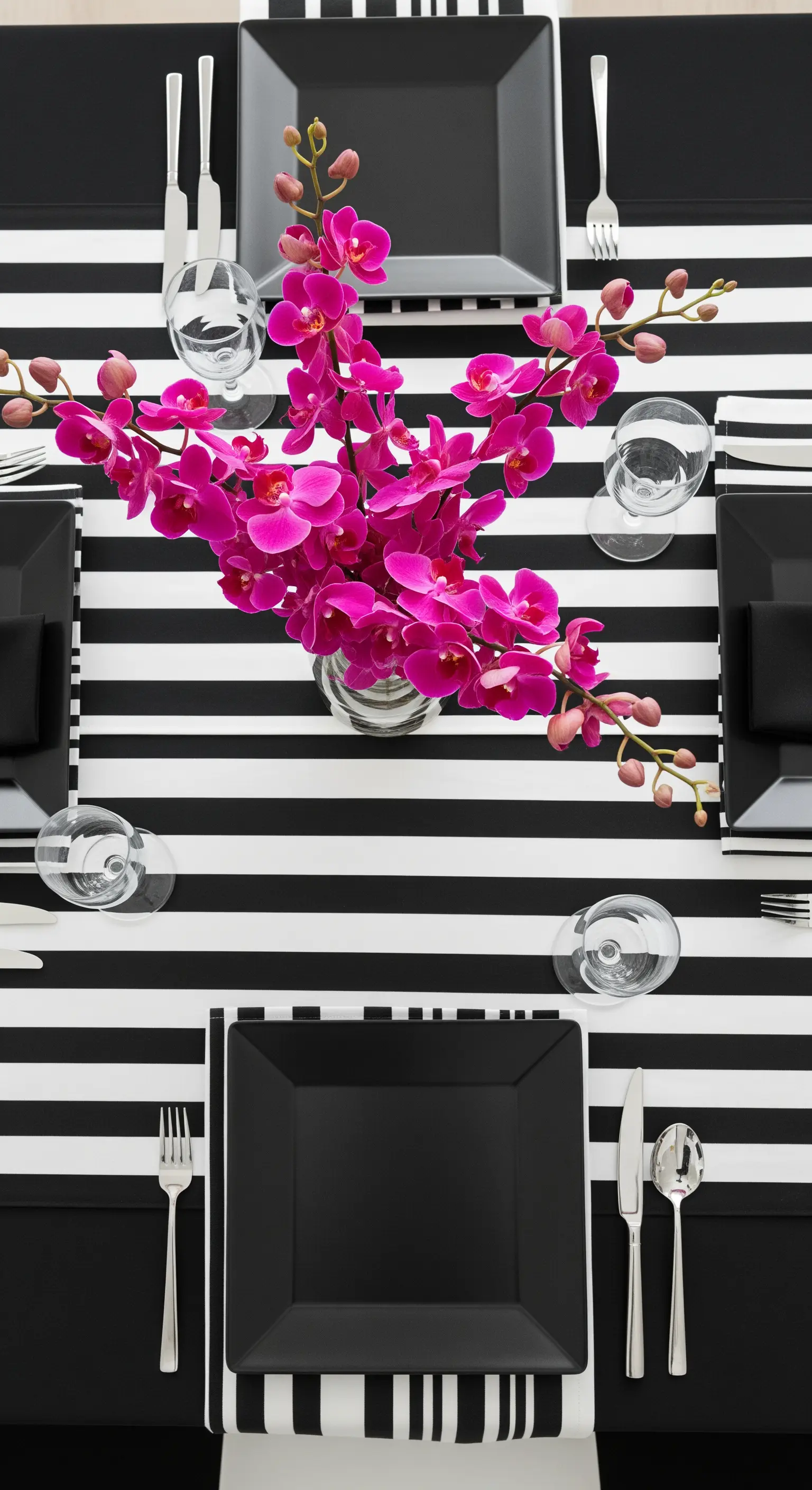 Tavola moderna con tovaglia a righe bianche e nere, piatti neri quadrati e un vaso di orchidee fucsia.