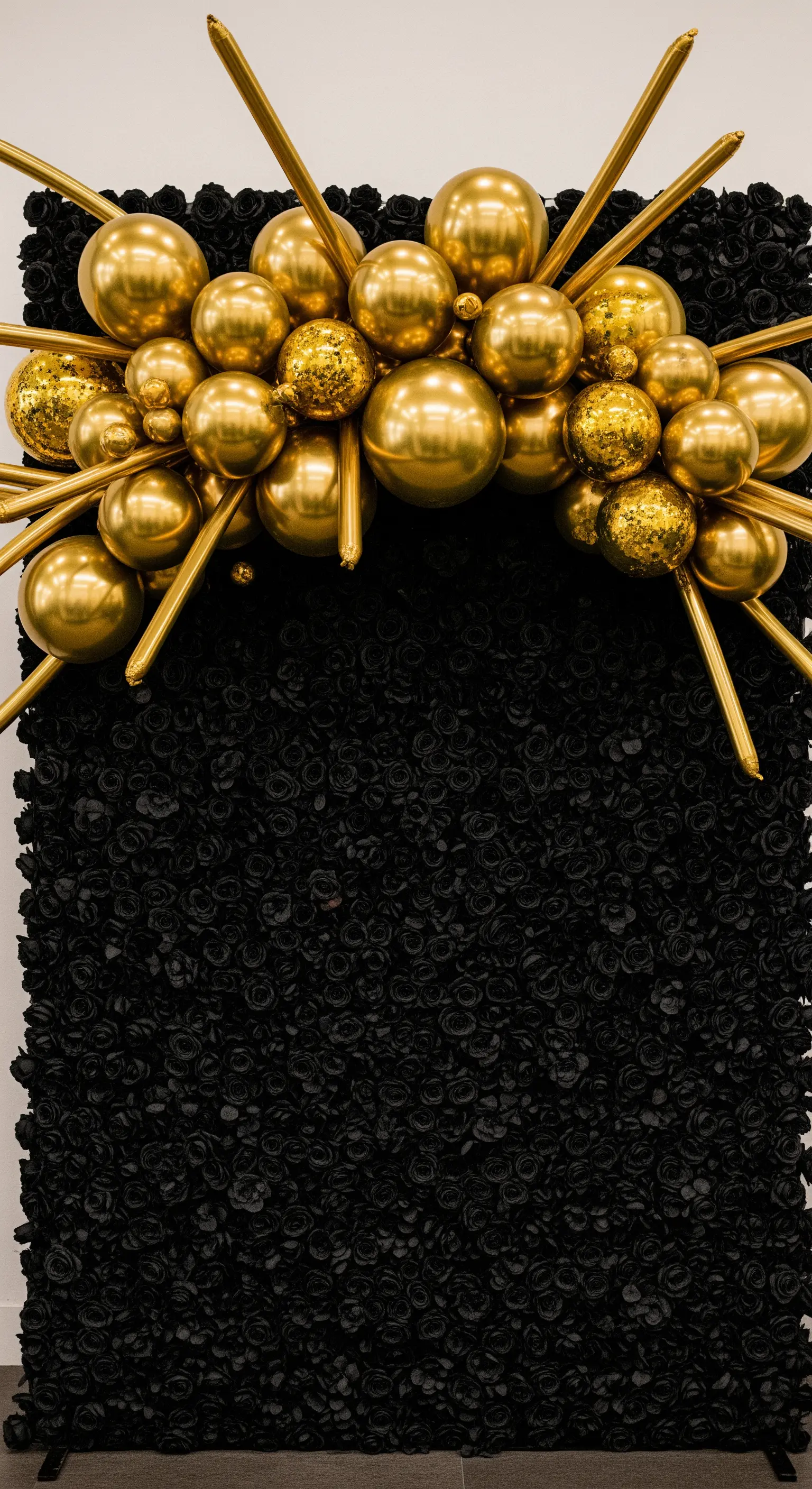 Parete di rose nere sormontata da una scultura di palloncini dorati lucidi.