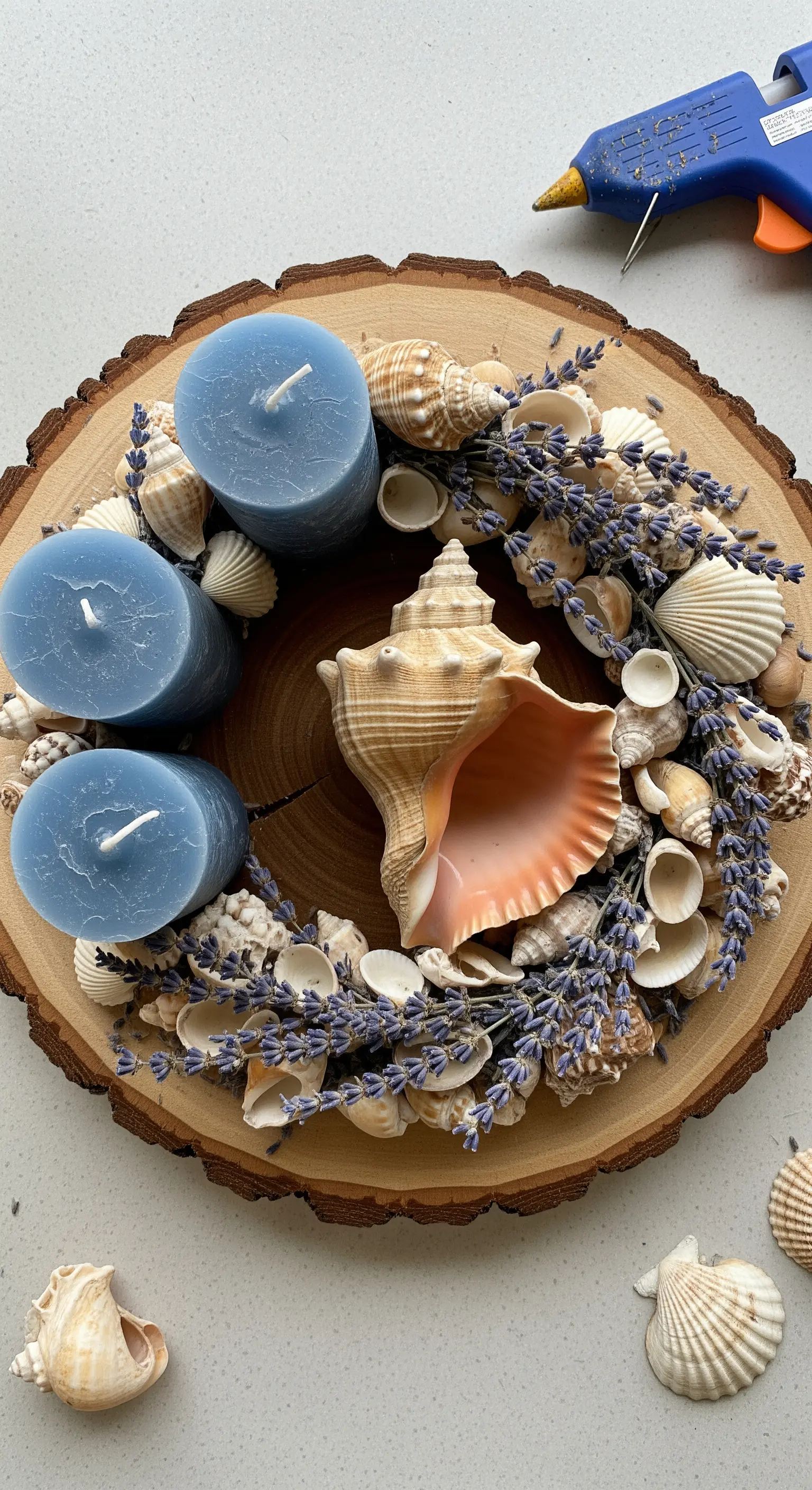 Sezione di tronco con tre candele blu circondate da una corona di conchiglie e lavanda.