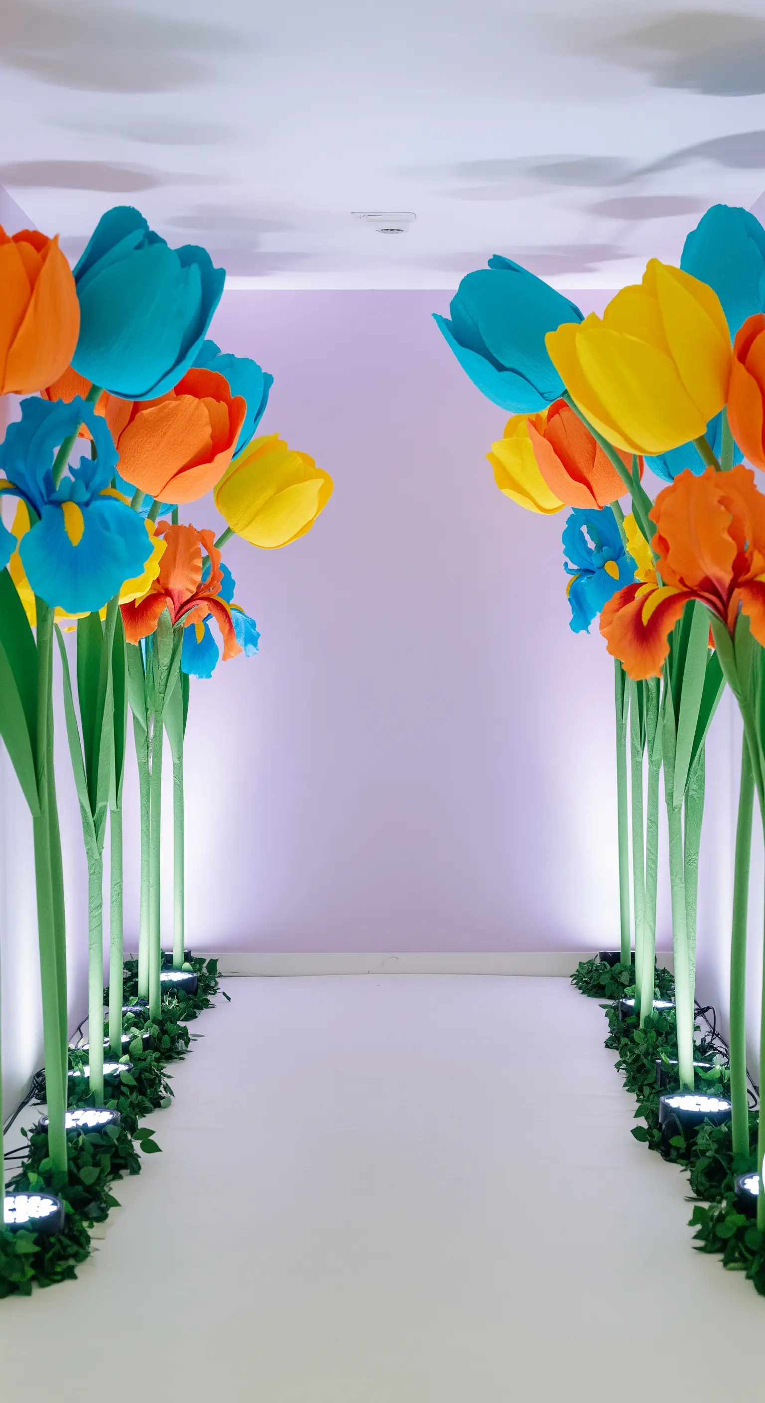 Ingresso scenografico con tulipani e iris di carta giganti illuminati dal basso.