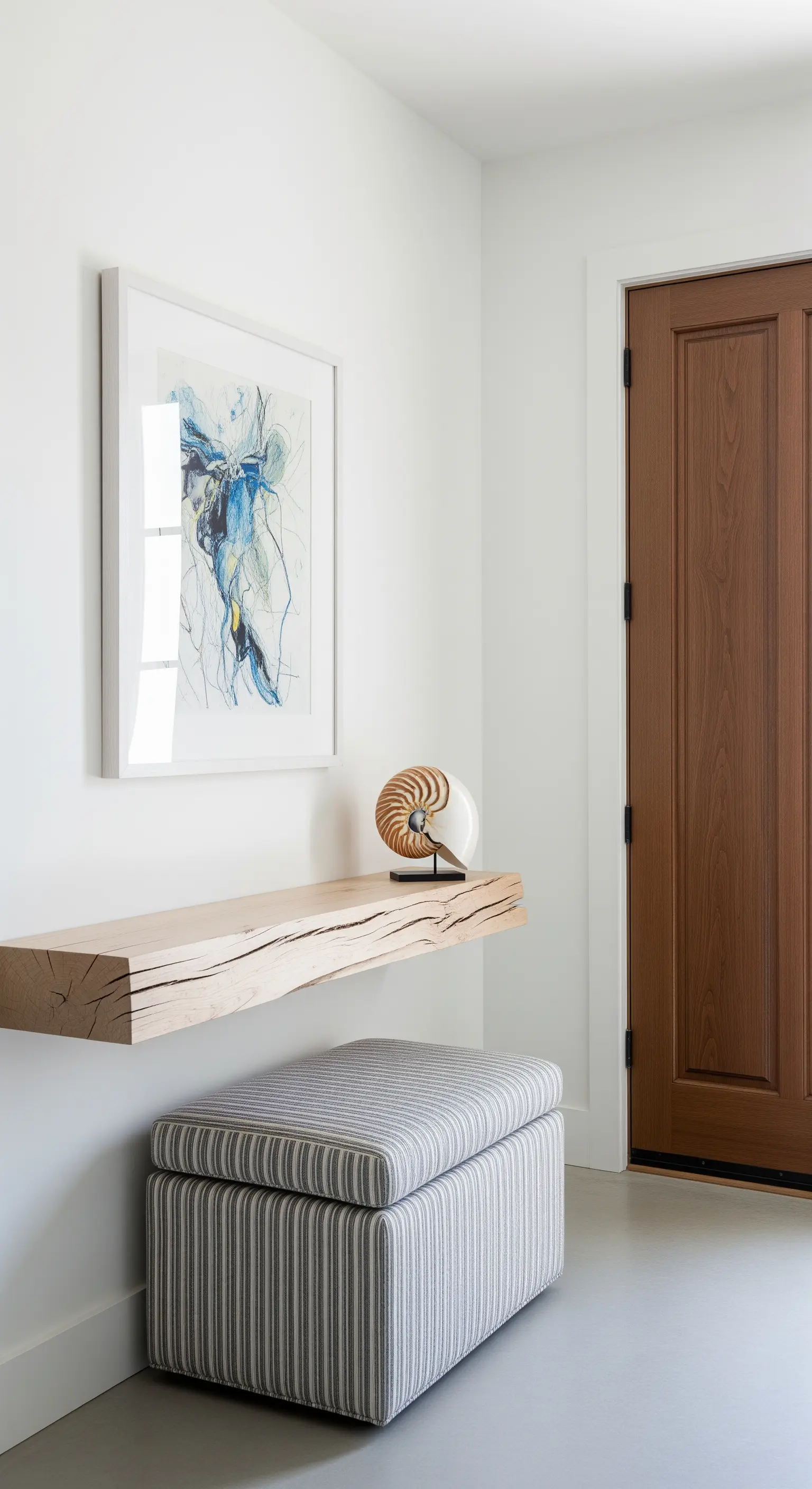 Angolo d'ingresso con mensola sospesa in legno grezzo e pouf contenitore a righe.