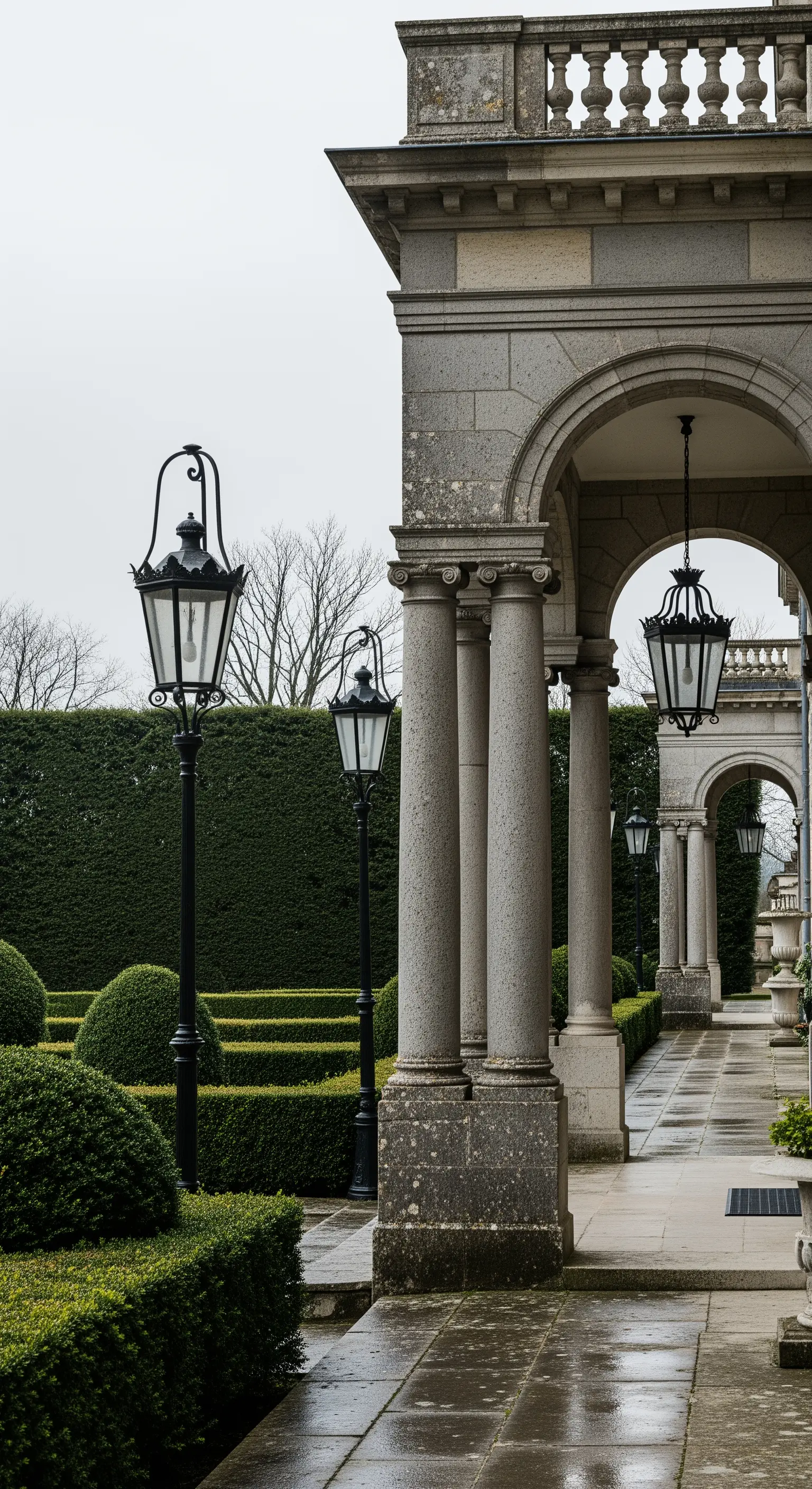 Lungo portico in pietra con colonne, archi e una fila di lampioni classici in ferro battuto