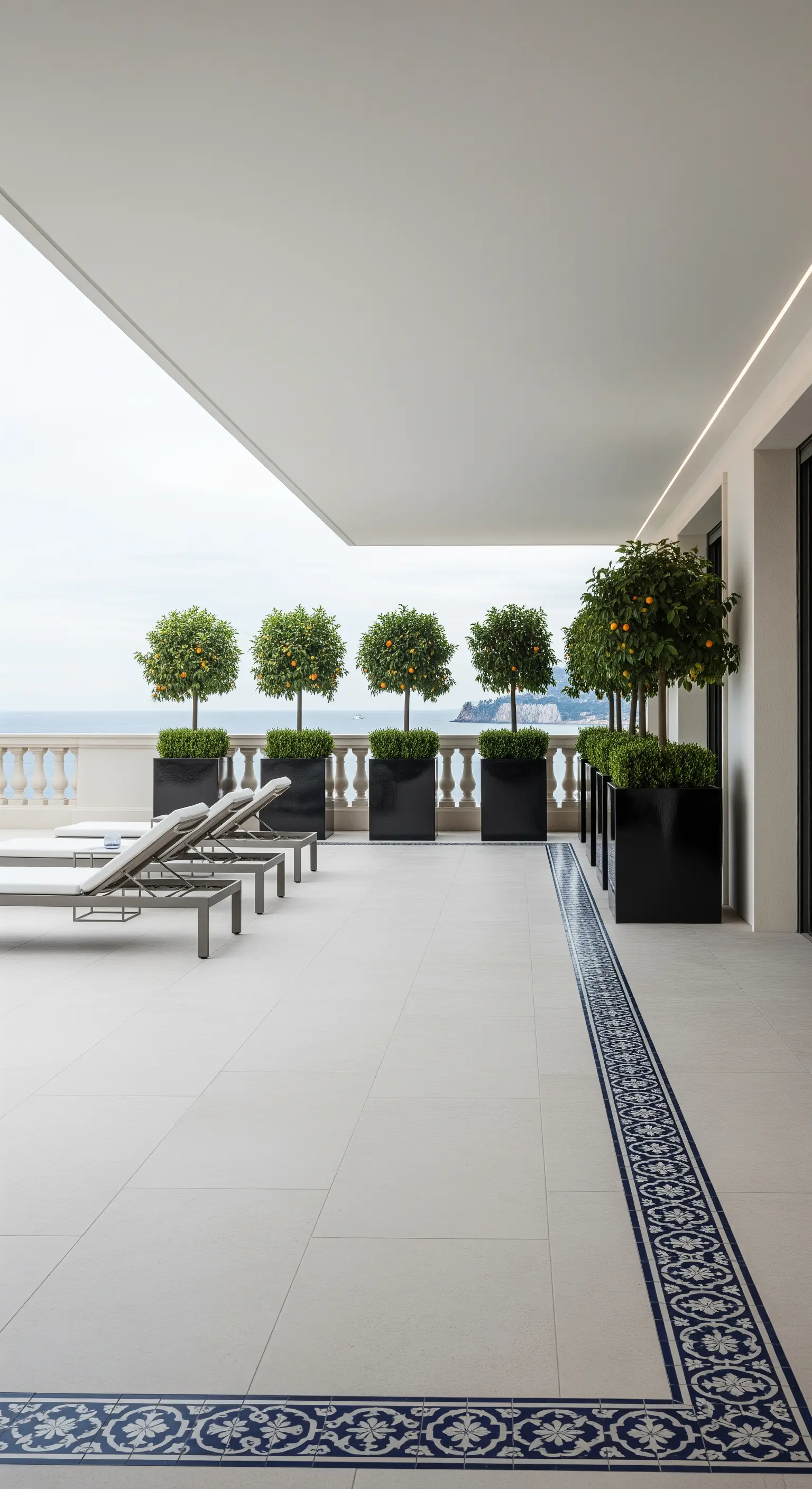 Terrazza moderna con pavimento bianco e bordo perimetrale in maioliche blu, con lettini e vasi neri