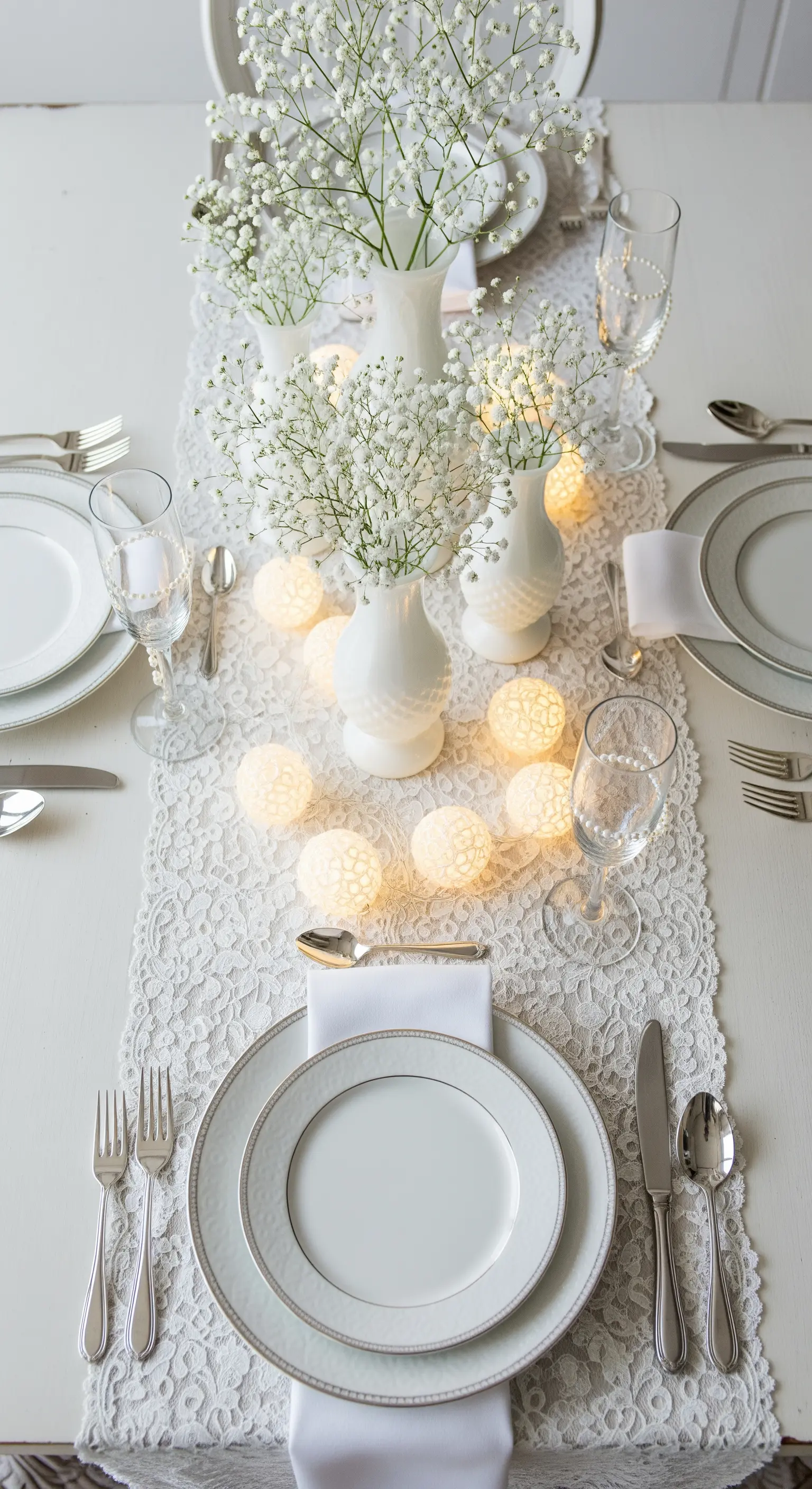 Tavola bianca con runner in pizzo, fiori di nebbiolina e sfere luminose in cotone.