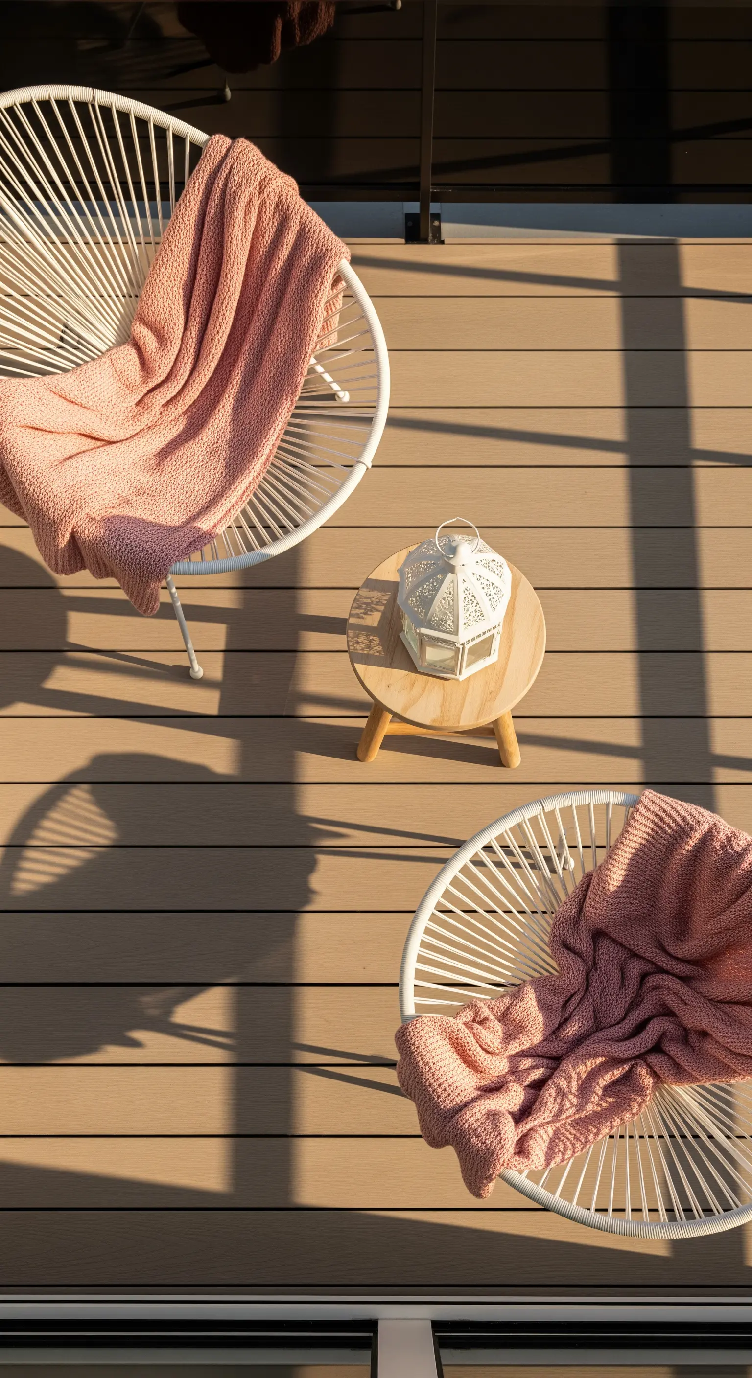 Due sedie bianche a filo con plaid rosa, viste dall'alto su un pavimento in legno.
