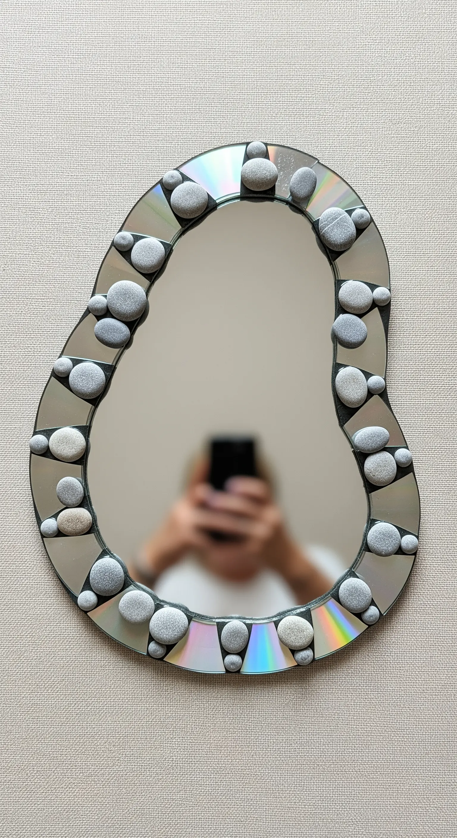 Specchio di forma organica con cornice decorata da CD e ciottoli di fiume grigi.
