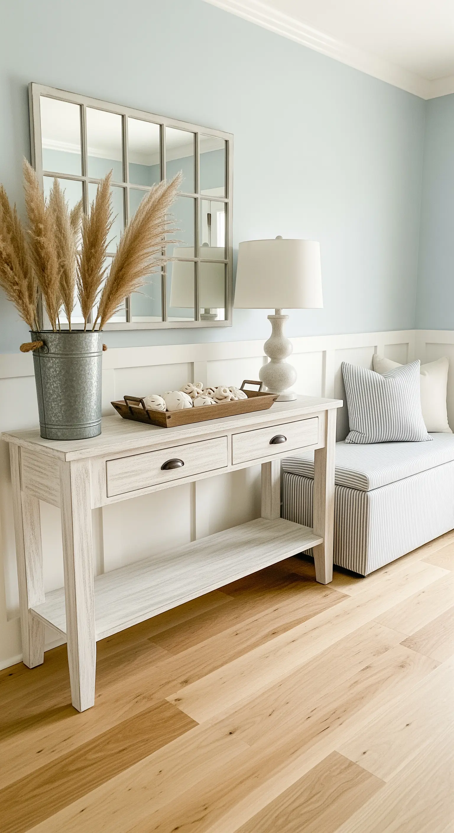 Ingresso con pareti azzurro polvere, boiserie bianca e consolle in legno sbiancato.