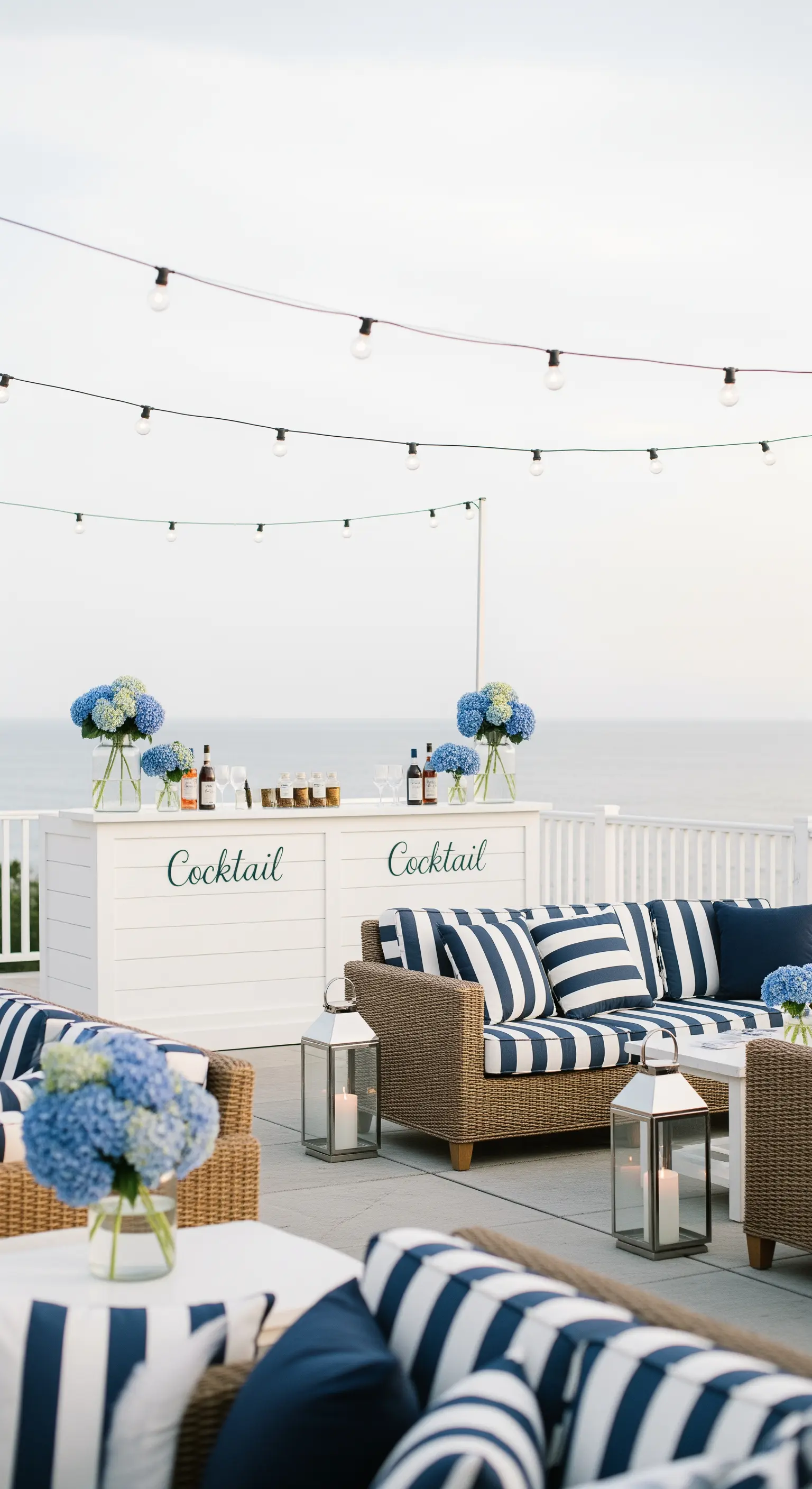 Terrazza vista mare in stile Hamptons con divani a righe, ortensie blu e lanterne.