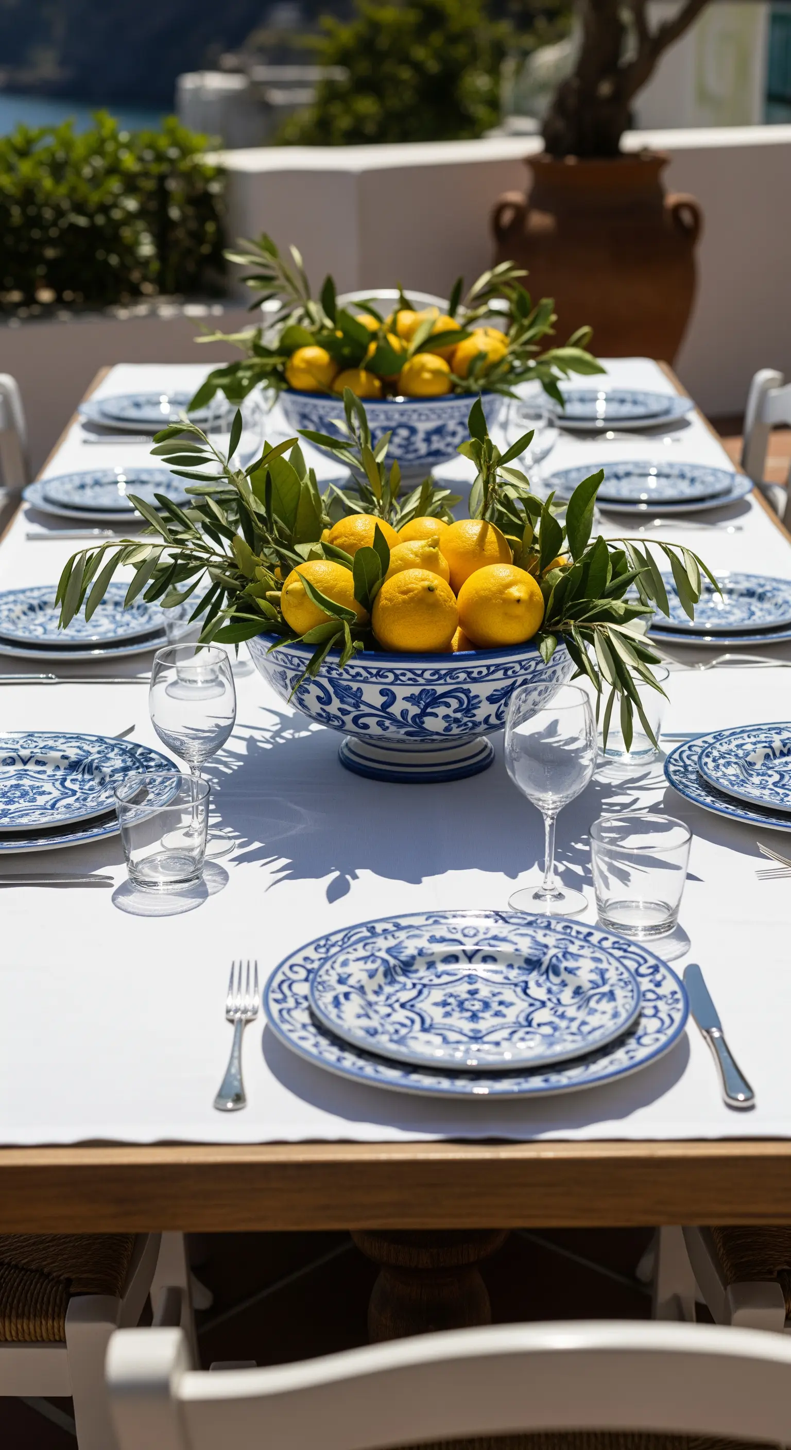 Tavola estiva con piatti in ceramica blu e un grande centrotavola di limoni e ulivo.