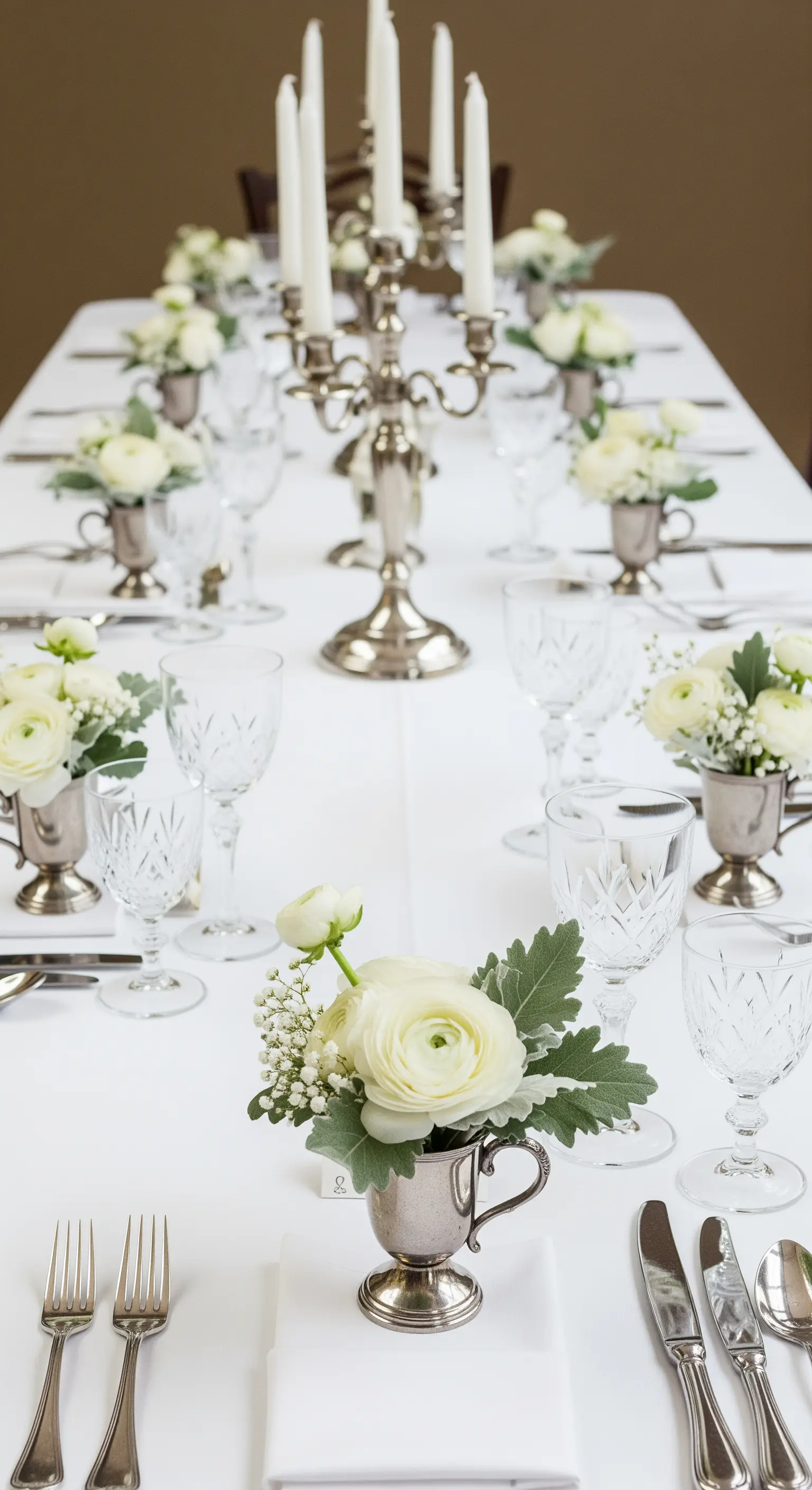Tavola bianca con piccoli bouquet di ranuncoli in coppe d'argento per ogni posto tavola.