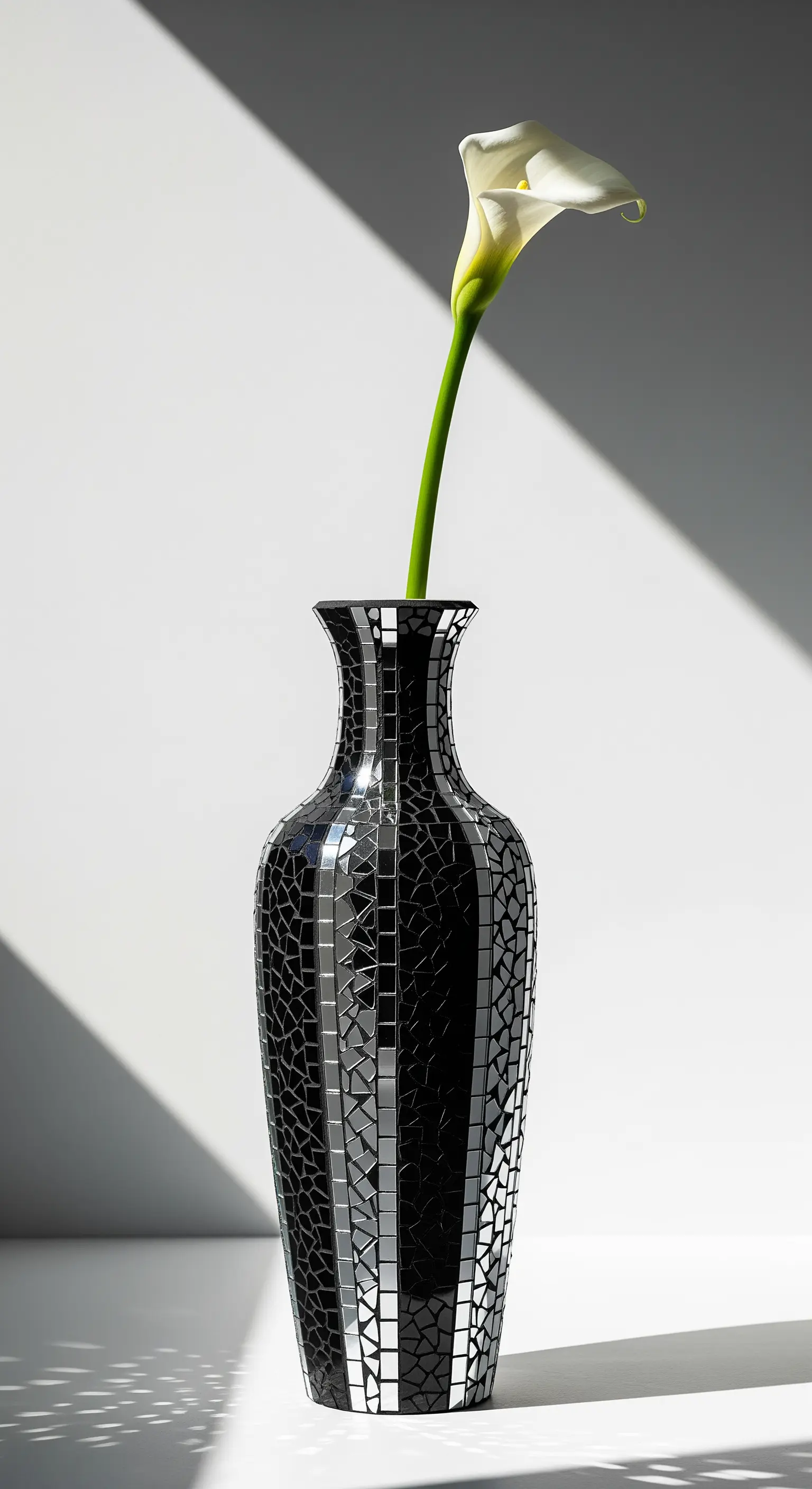 Vaso nero slanciato con un mosaico di specchi e vetro nero, contenente una singola calla bianca.