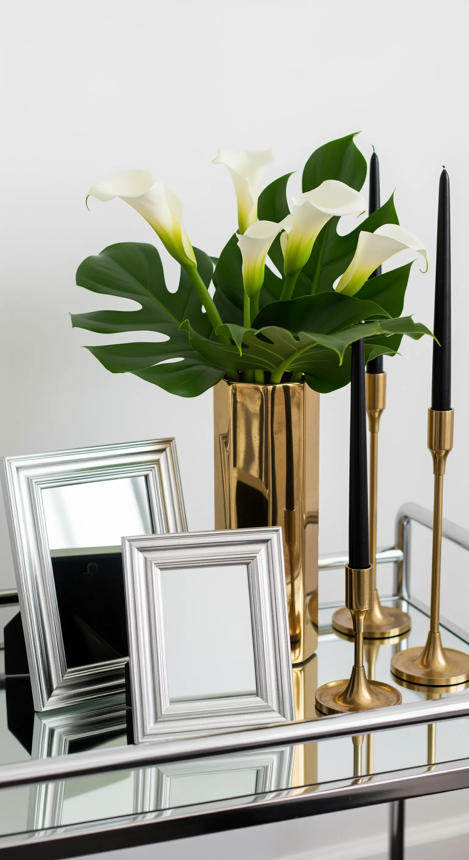 Carrello bar con calle bianche in un vaso dorato, candele nere e cornici d'argento.