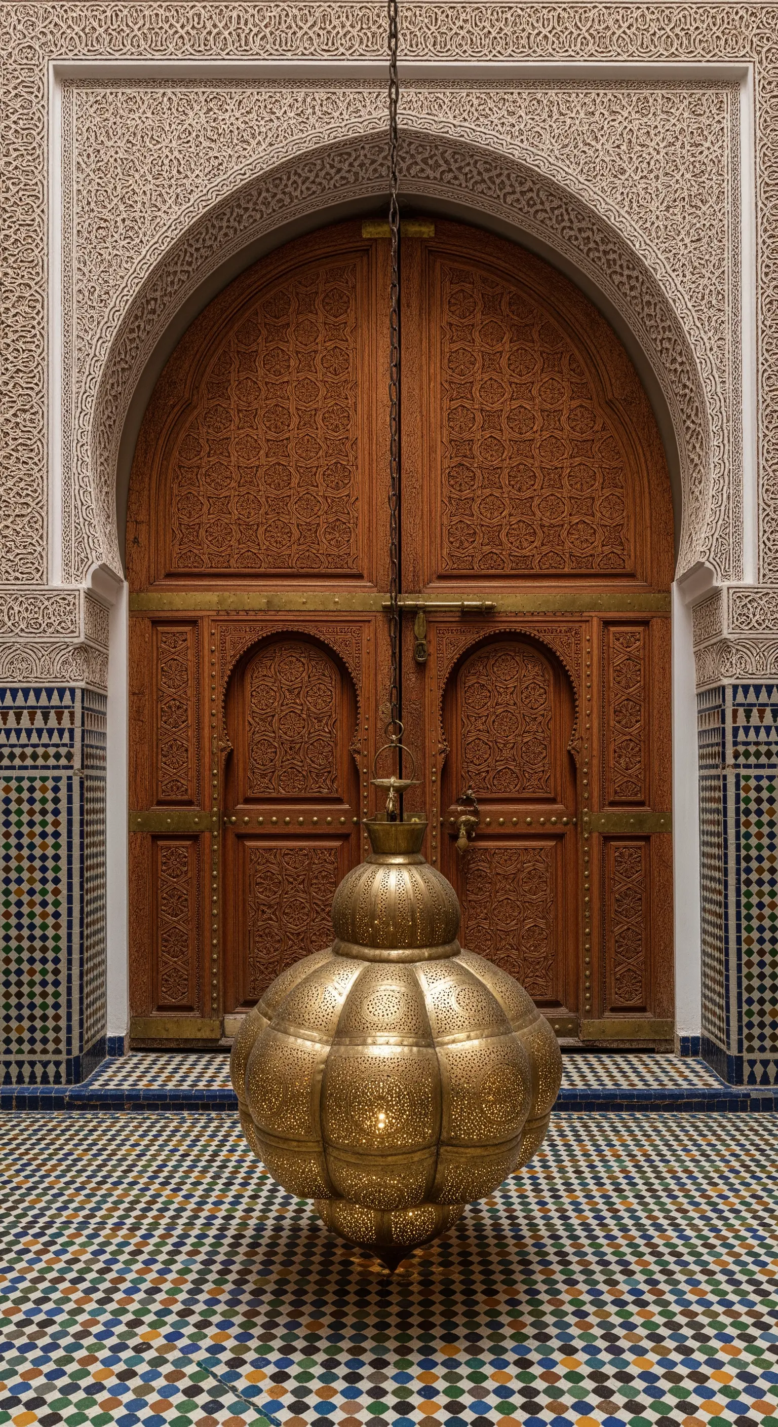 Ingresso marocchino con porta in legno intagliato, piastrelle zellige e una grande lanterna in ottone.