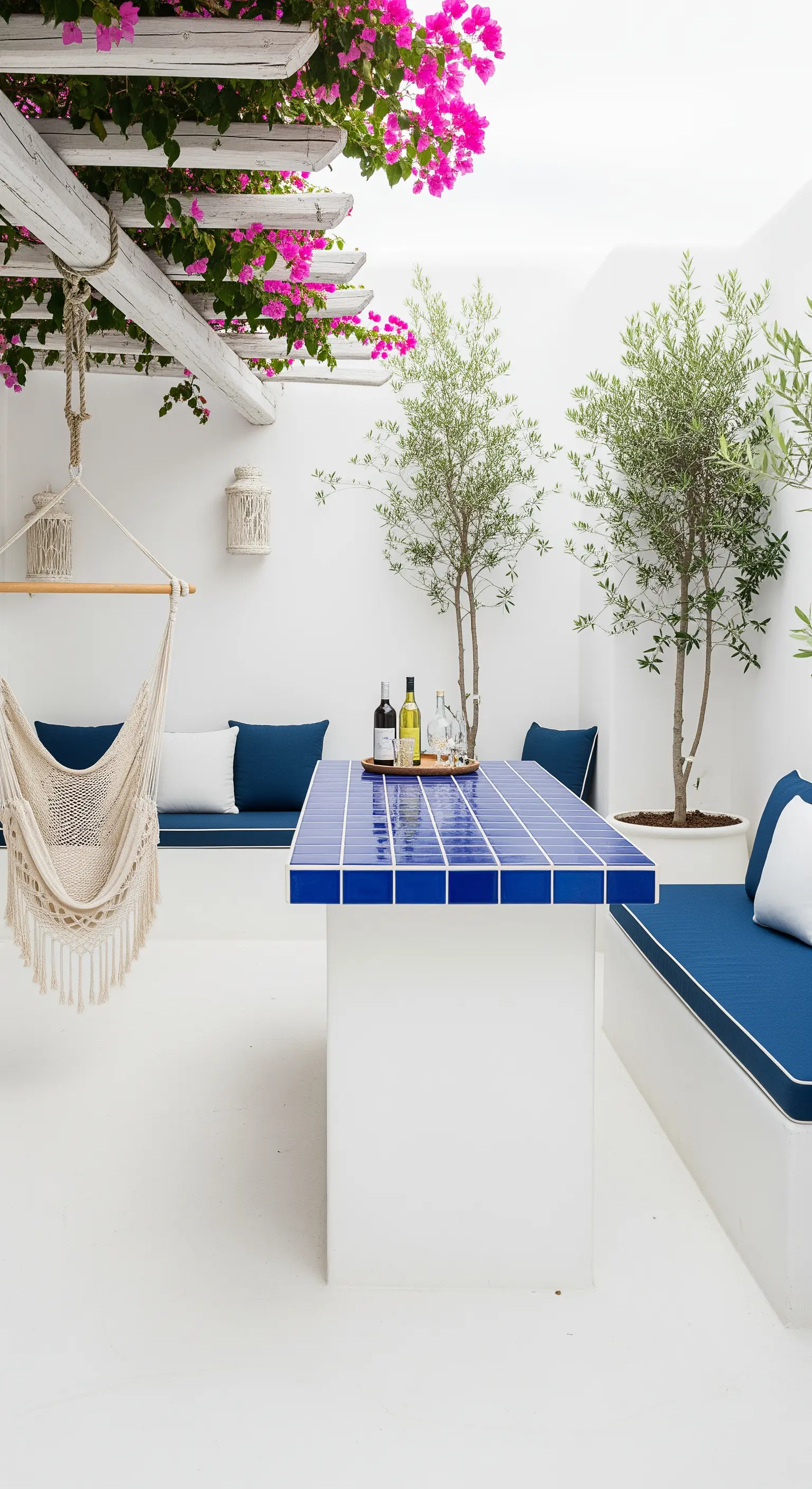 Patio bianco in stile greco con tavolo-bar piastrellato di blu, bouganville e sedia sospesa.