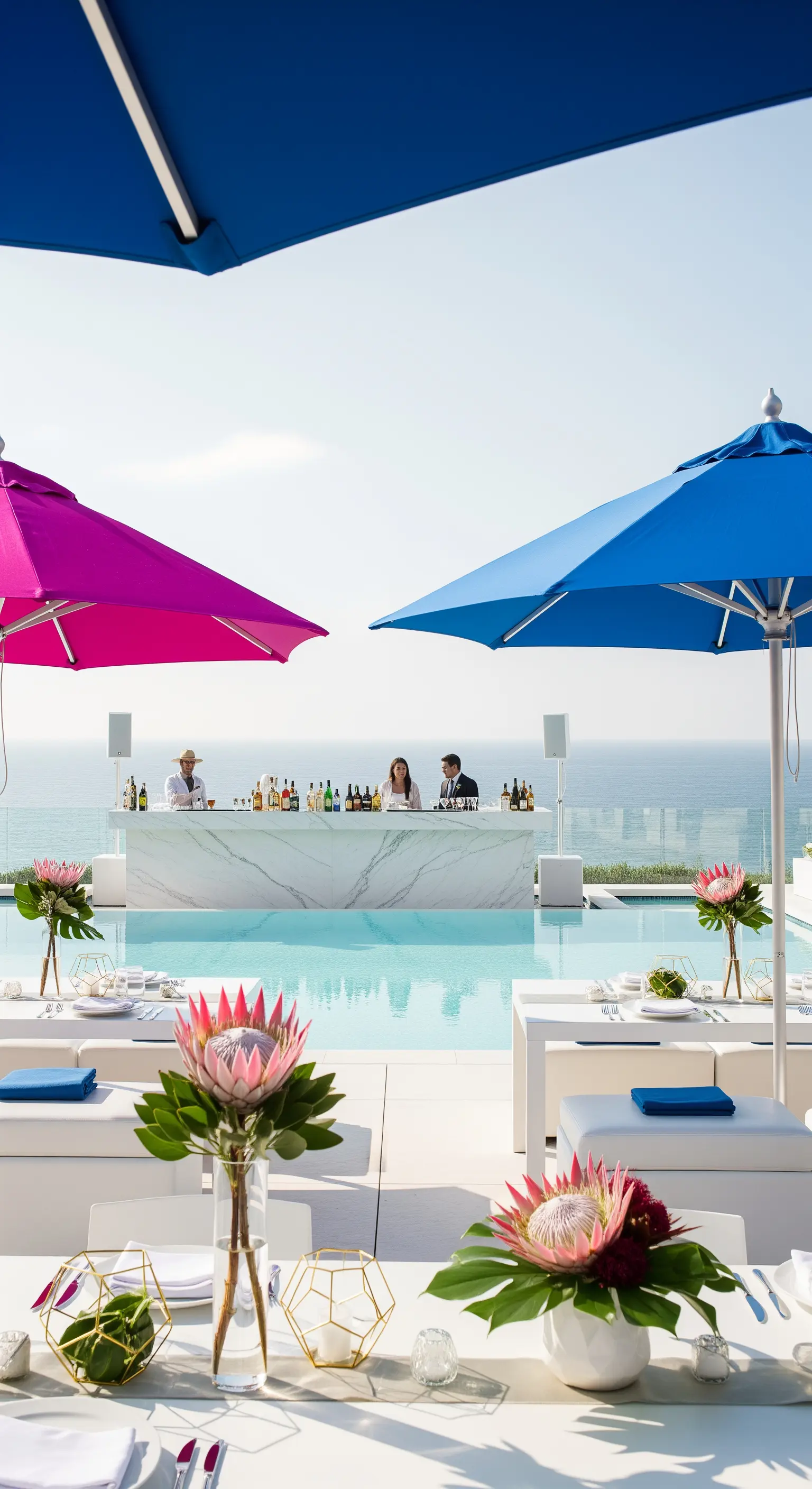 Party a bordo piscina con bar in marmo, ombrelloni fucsia e blu e centrotavola con protee