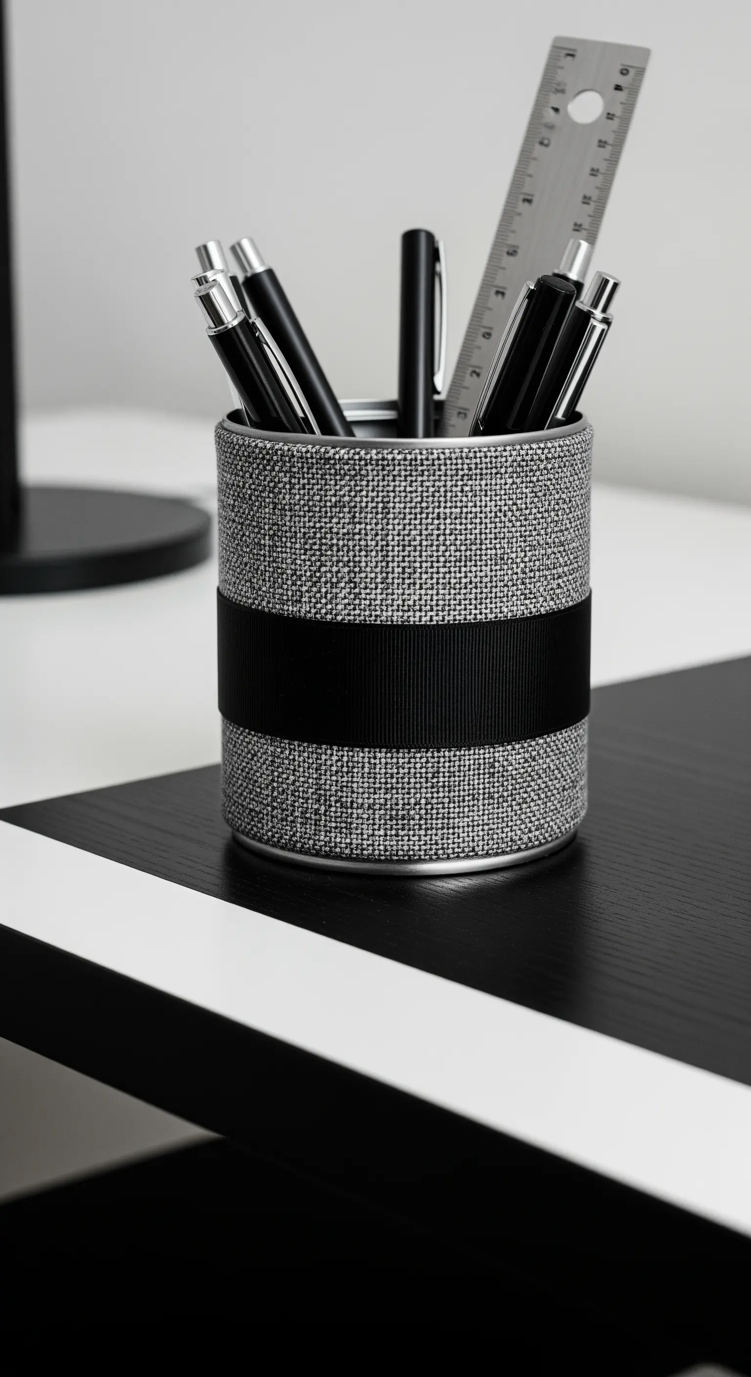 Portapenne grigio con una fascia nera, posizionato su una scrivania in bianco e nero.