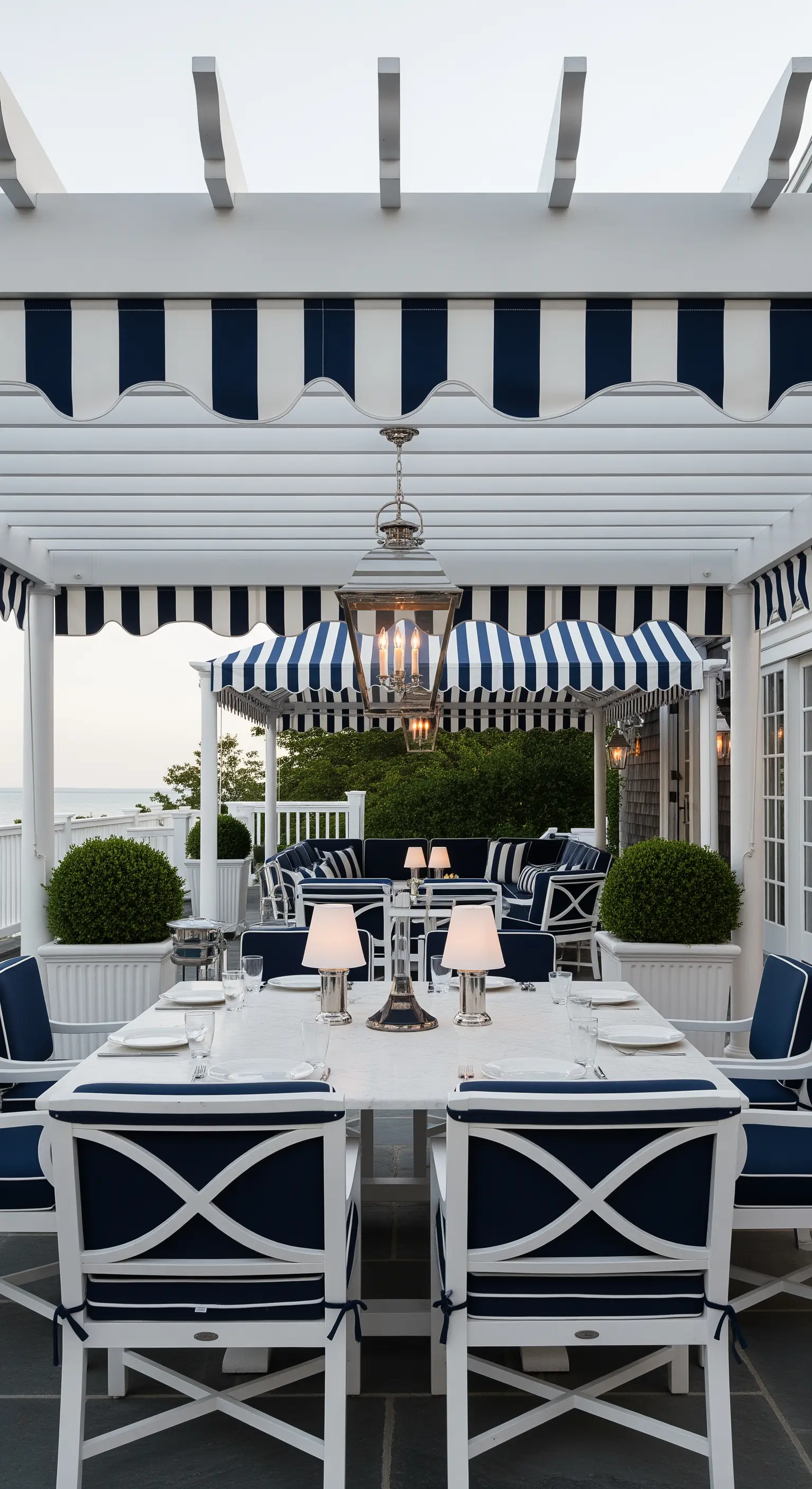 Patio in stile nautico con pergola bianca, tende a righe blu e arredi coordinati.