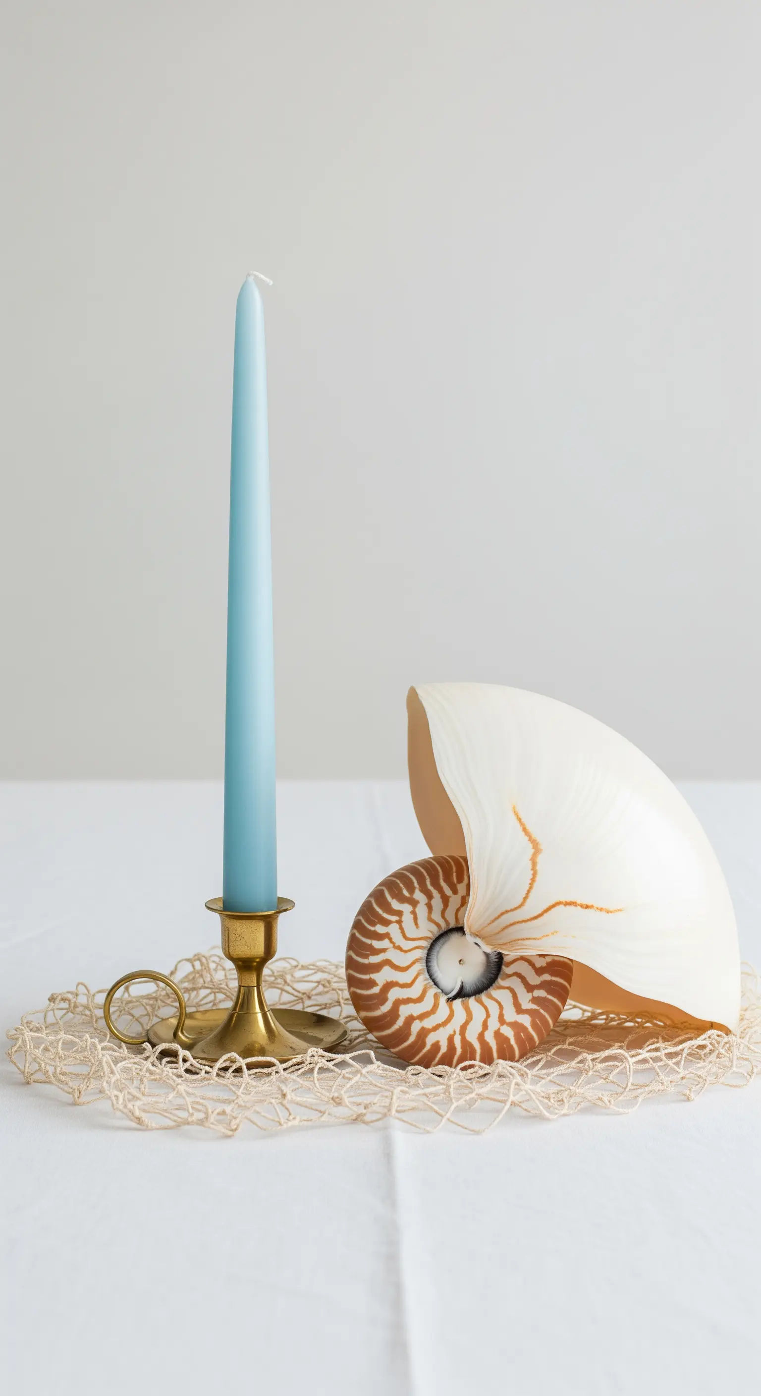 Composizione minimalista con conchiglia Nautilus, candela azzurra e portacandele in ottone