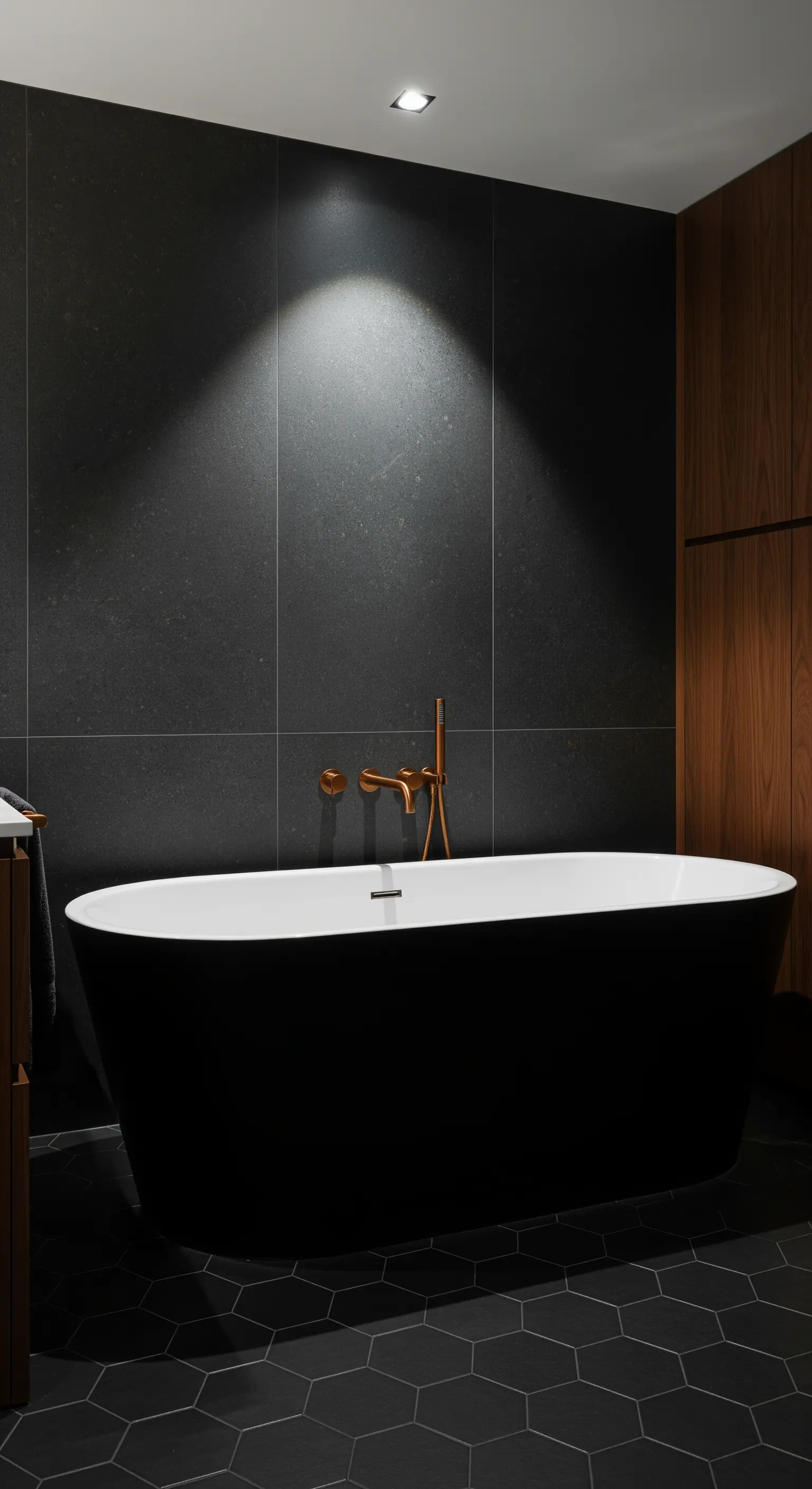 Vasca freestanding nera in un bagno scuro con rubinetteria in rame e luce d'accento.