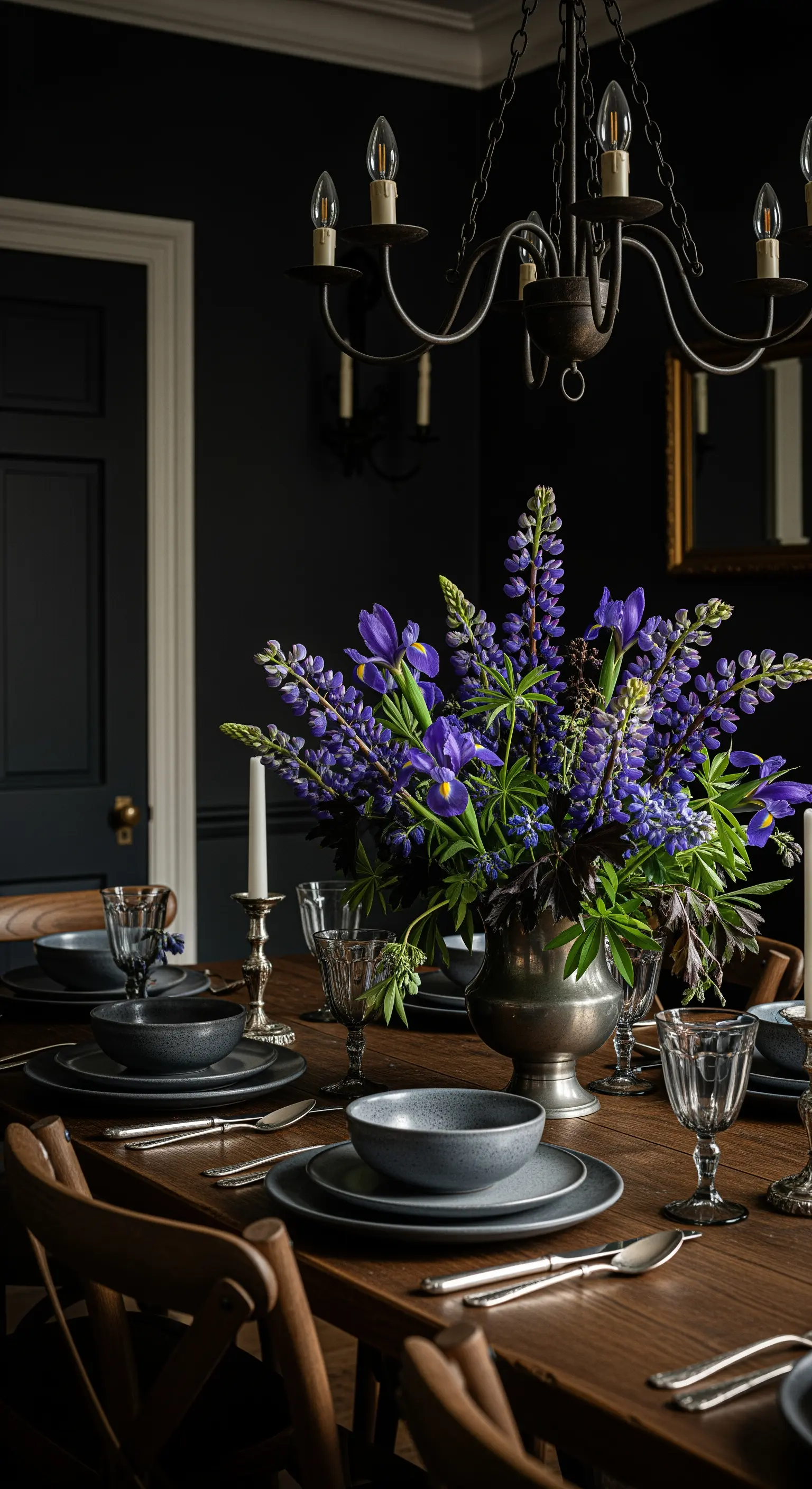 Tavola in una sala da pranzo scura con un grande bouquet di fiori viola in un vaso d'argento