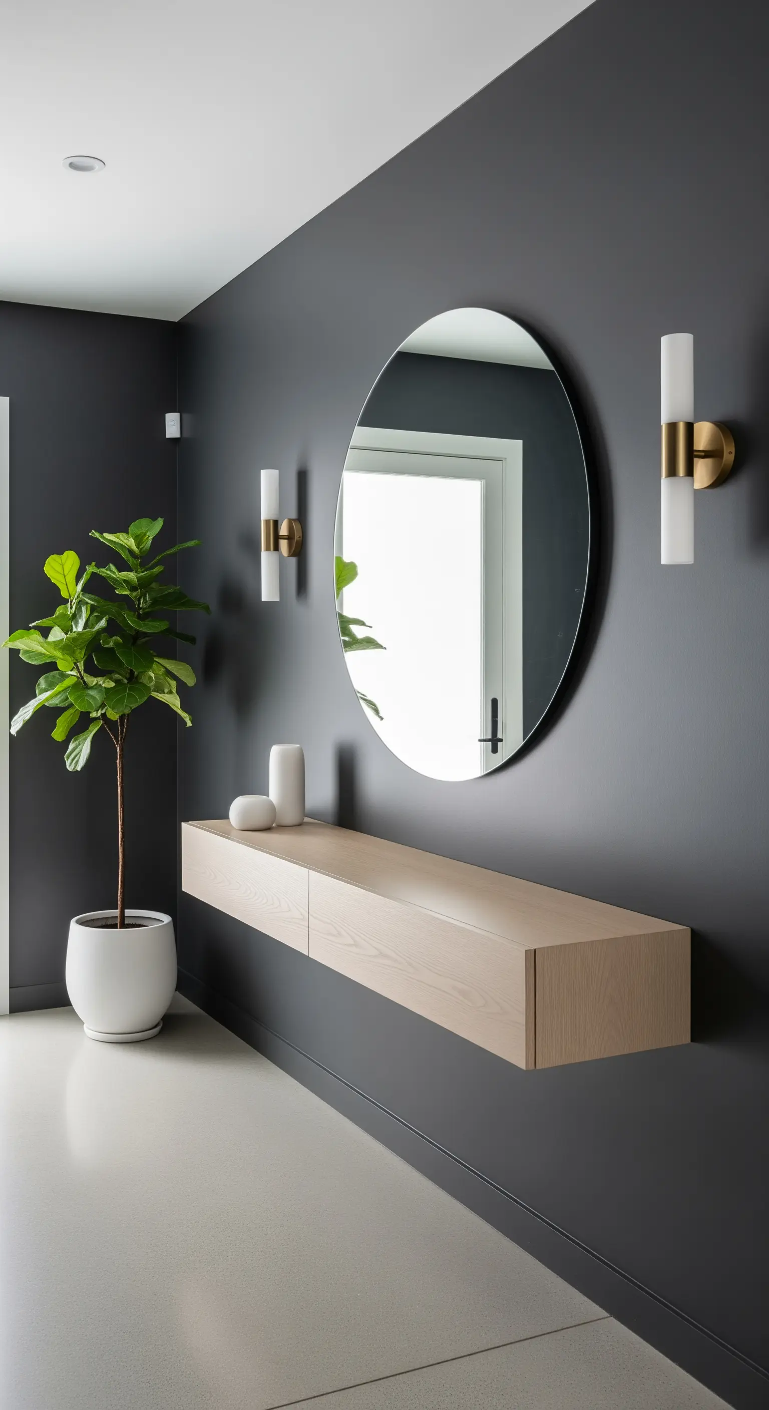 Ingresso minimal con parete grigio antracite, consolle sospesa in legno chiaro e specchio rotondo.