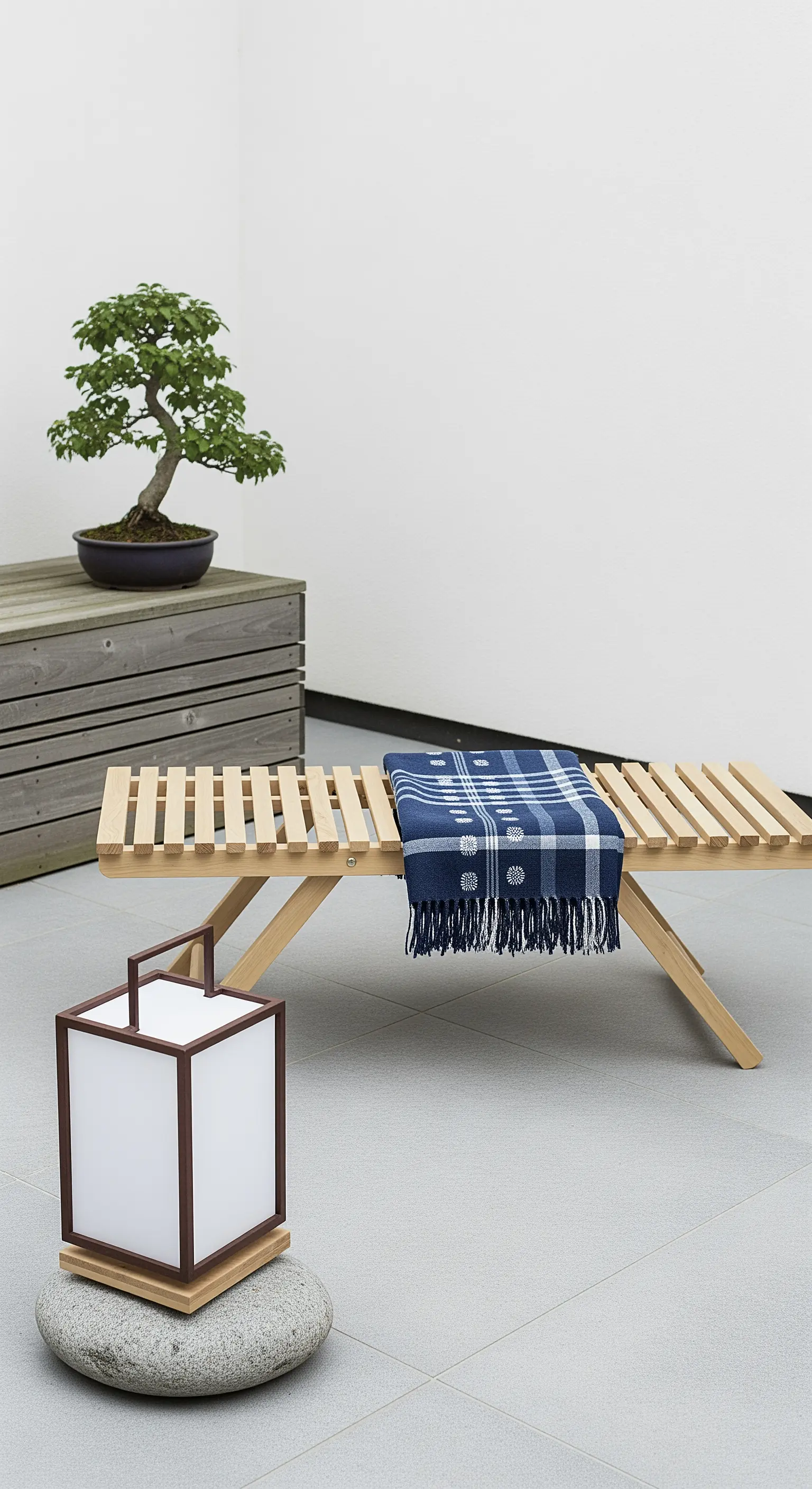 Panca bassa in legno con plaid blu, lanterna su una pietra e un albero di bonsai.