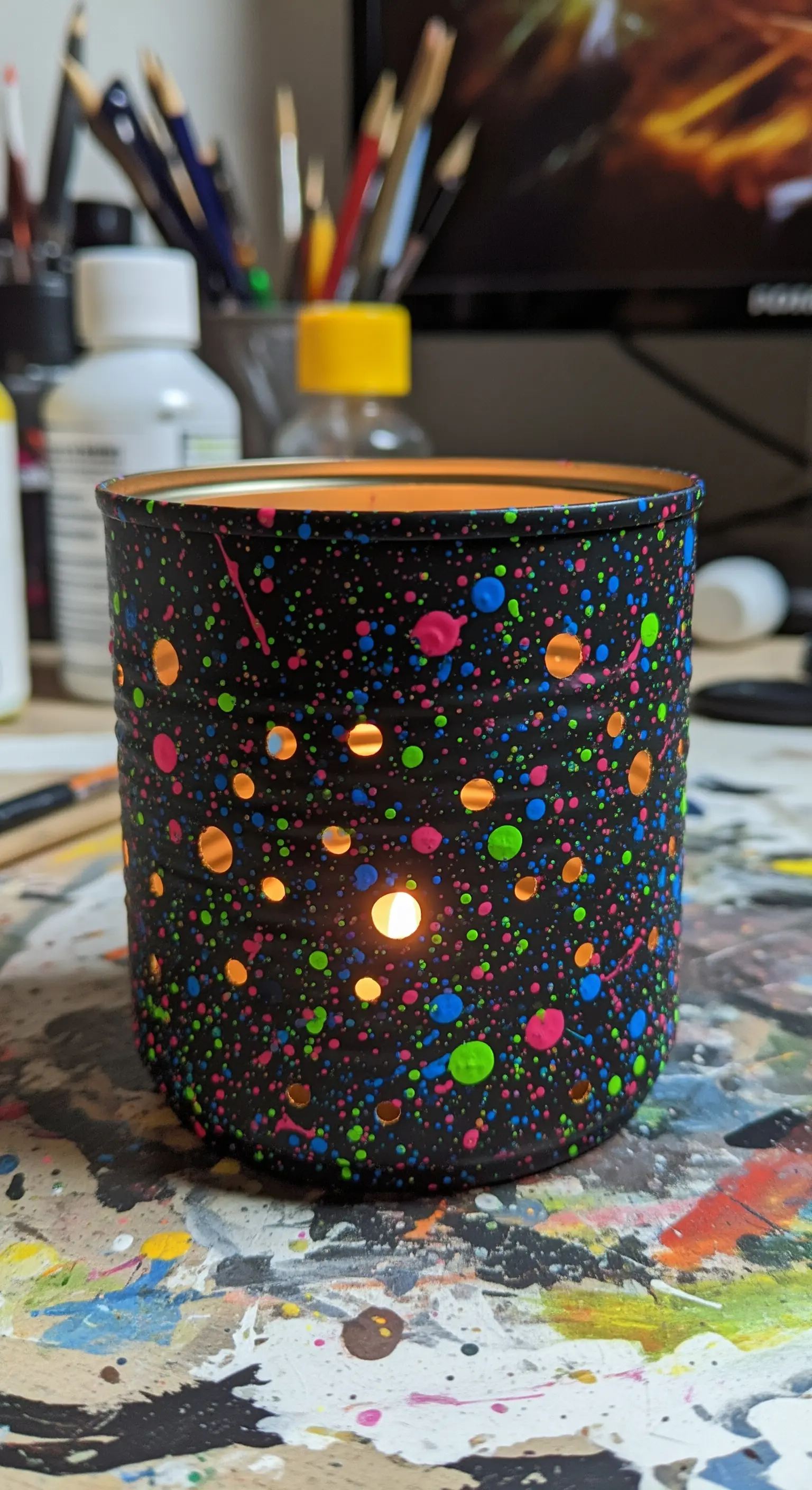 Portacandela nero con schizzi di vernice neon colorata e fori rotondi.