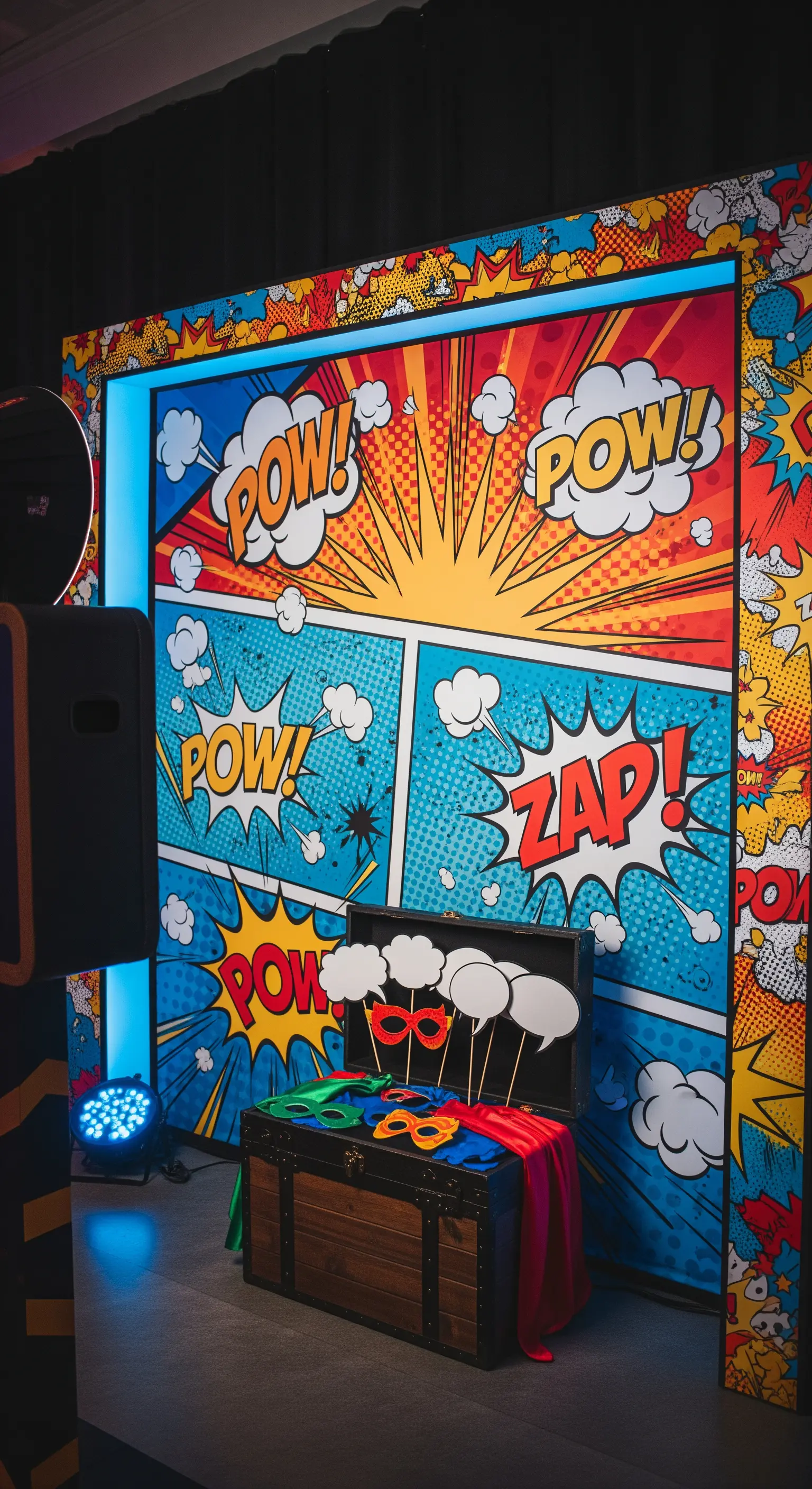 Photo booth a tema fumetto con sfondo colorato, onomatopee e maschere da supereroe in un baule.