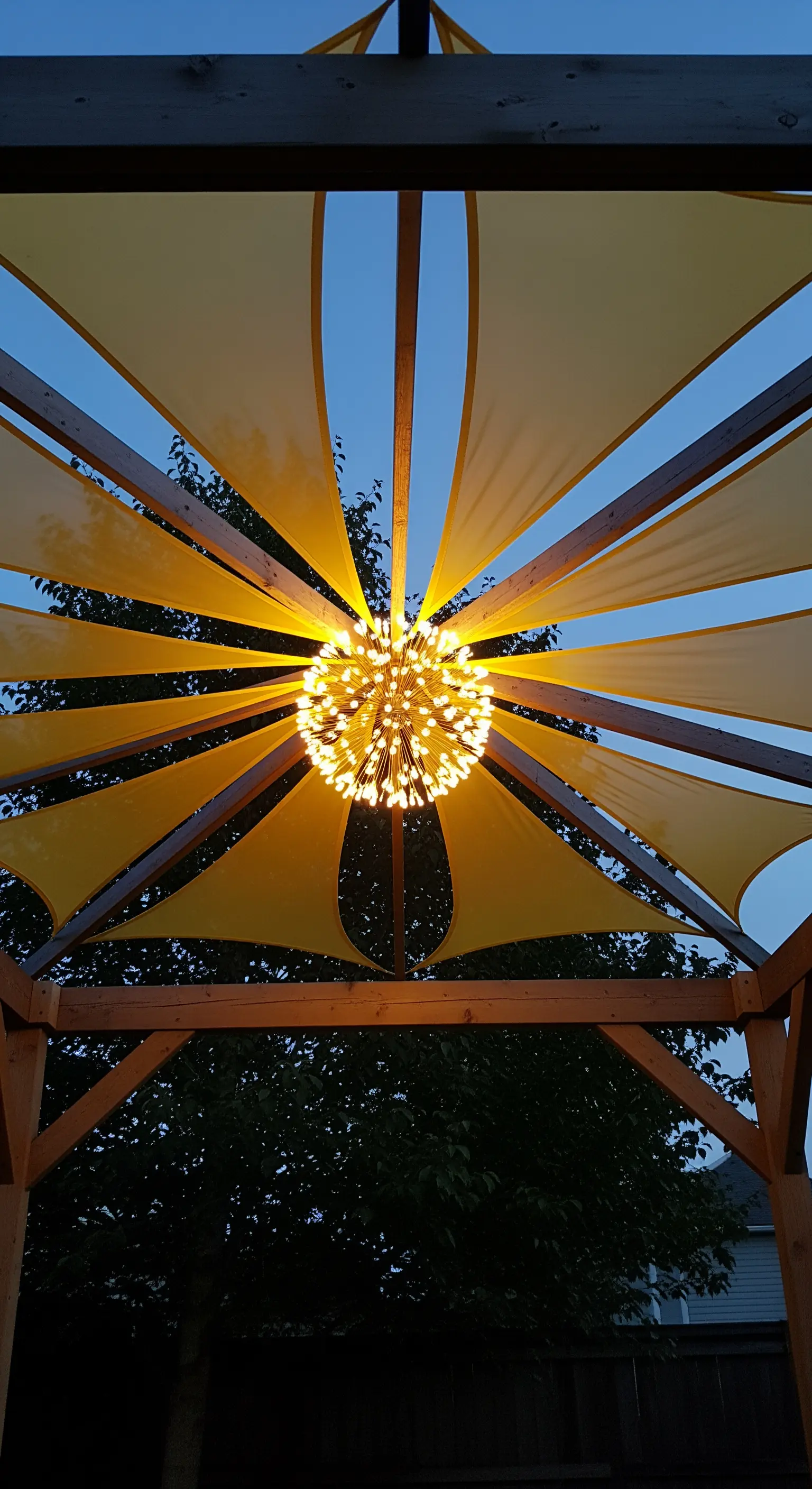 Vista dal basso di un pergolato con teli gialli e un lampadario a sfera.
