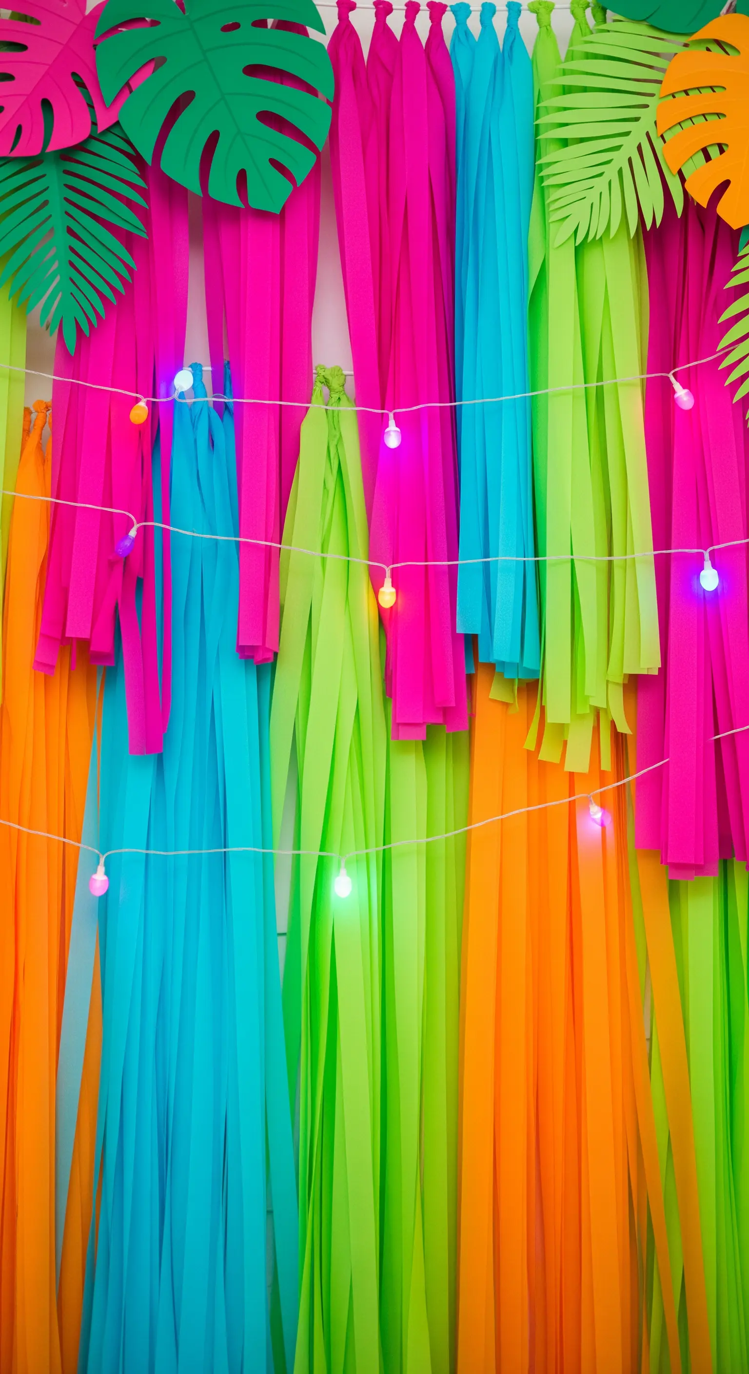 Fondale tropicale con frange di carta crespa color neon e foglie di cartoncino.