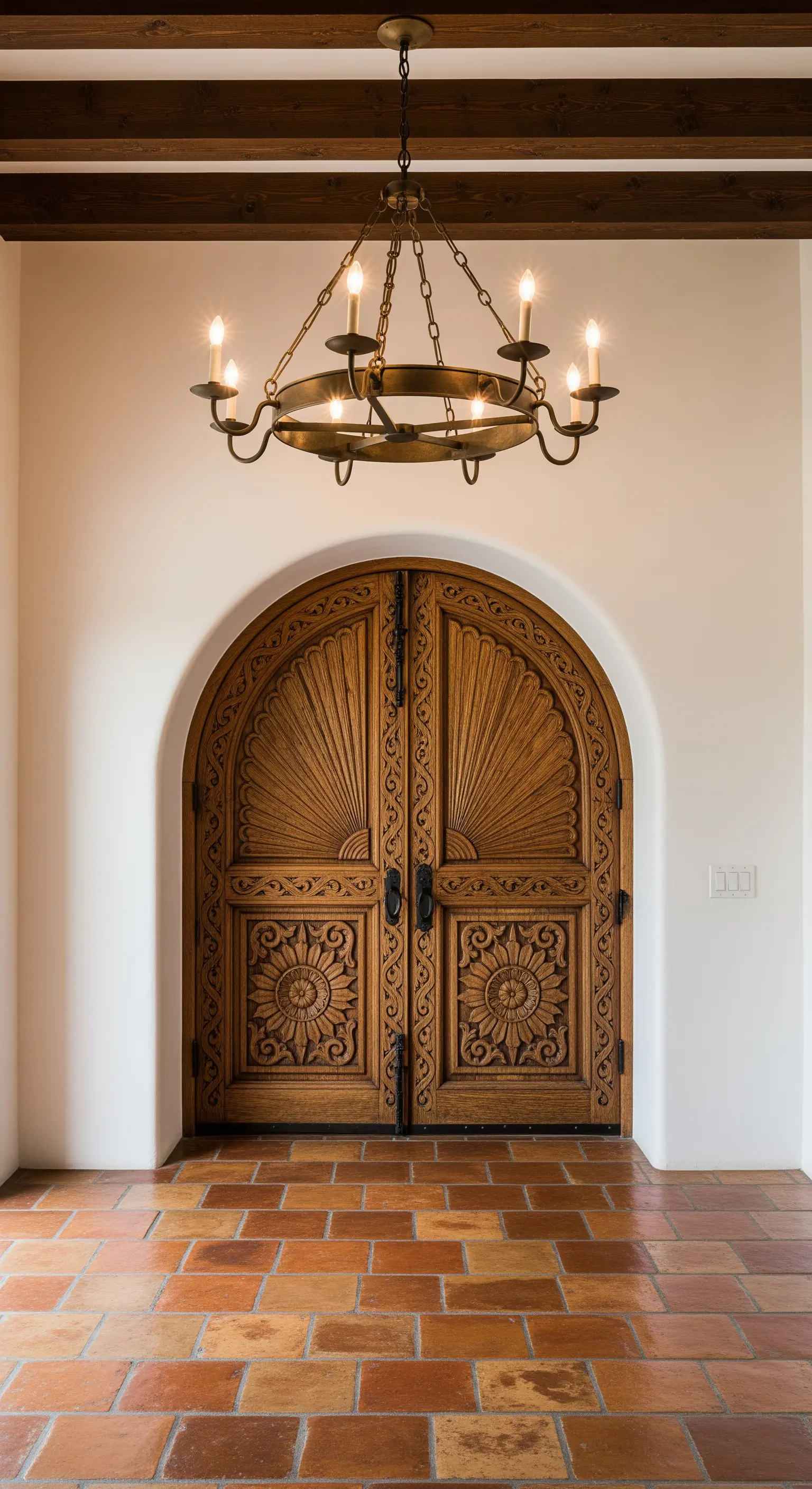 Ingresso in stile spagnolo con porta ad arco intagliata, pareti bianche e pavimento in cotto.