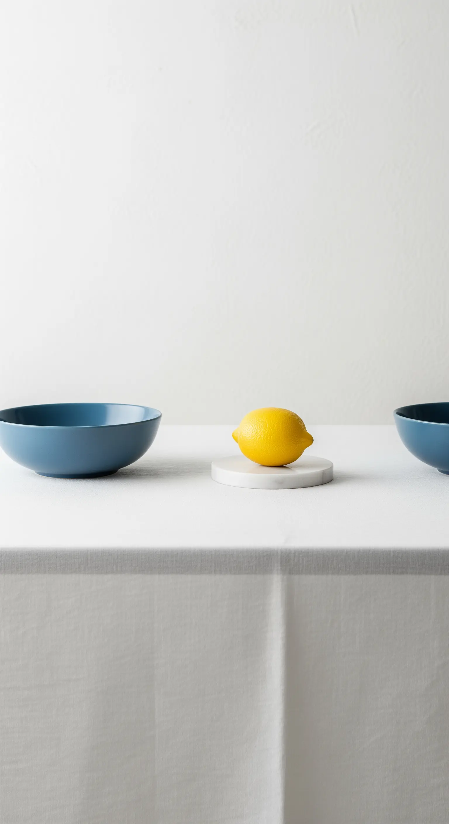 Allestimento minimalista con una ciotola blu, un limone singolo e una tovaglia bianca.