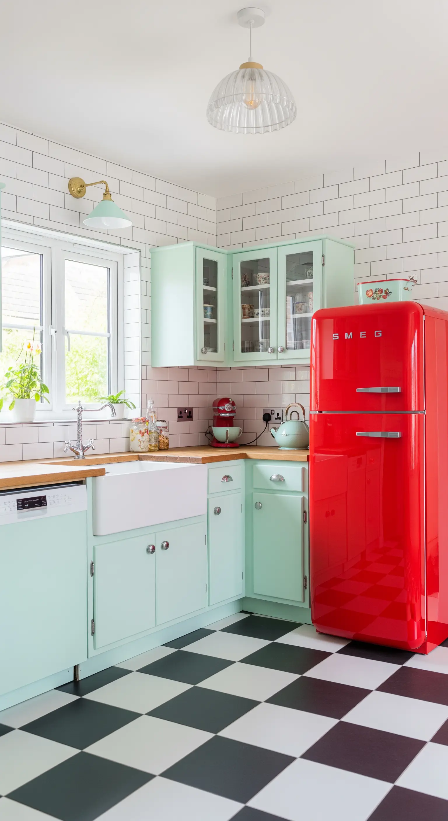 Cucina retrò con mobili verde menta, frigorifero rosso e pavimento a scacchi.