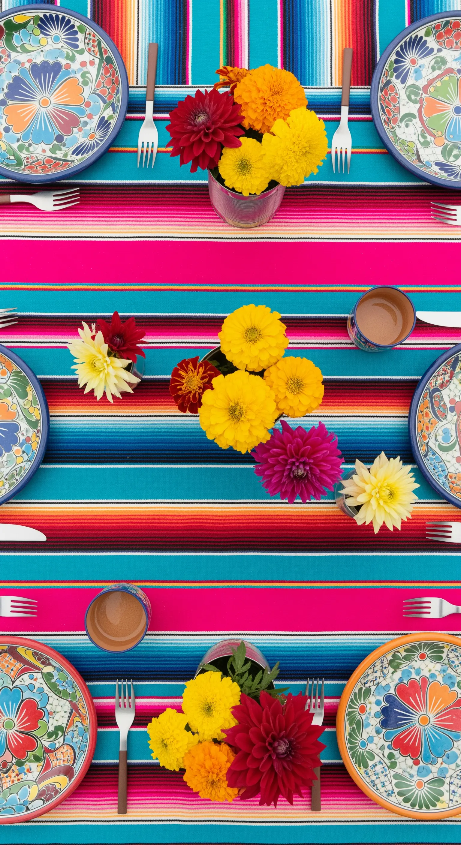 Tavola coloratissima con runner a righe messicane, piatti in ceramica dipinta e fiori di dalia.