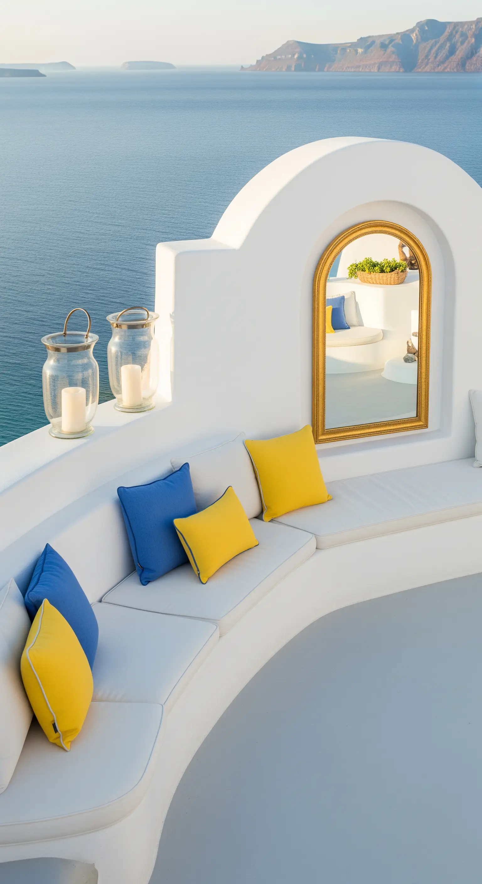 Terrazza bianca mediterranea con divano curvo, specchio dorato ad arco e cuscini blu e gialli.
